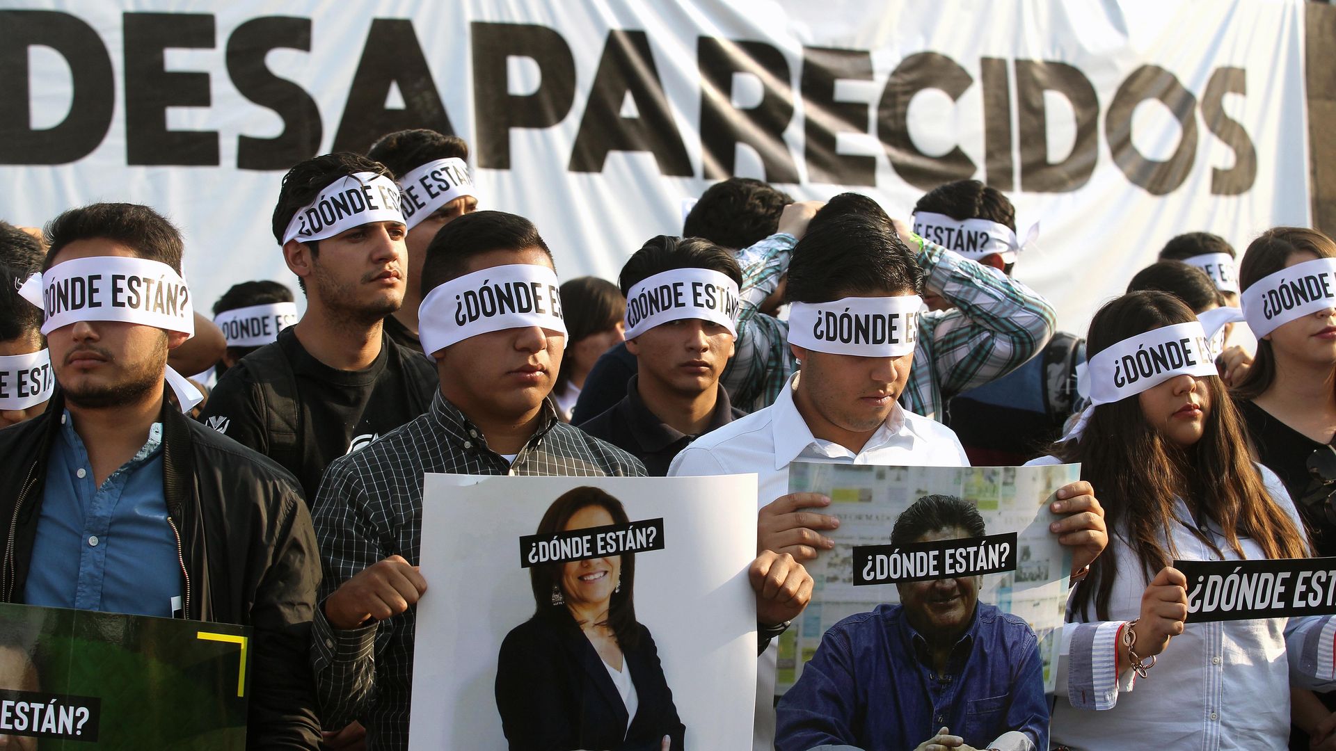 Several protesters with bands covering their eyes hold up pictures of people who have gone missing in Mexico 
