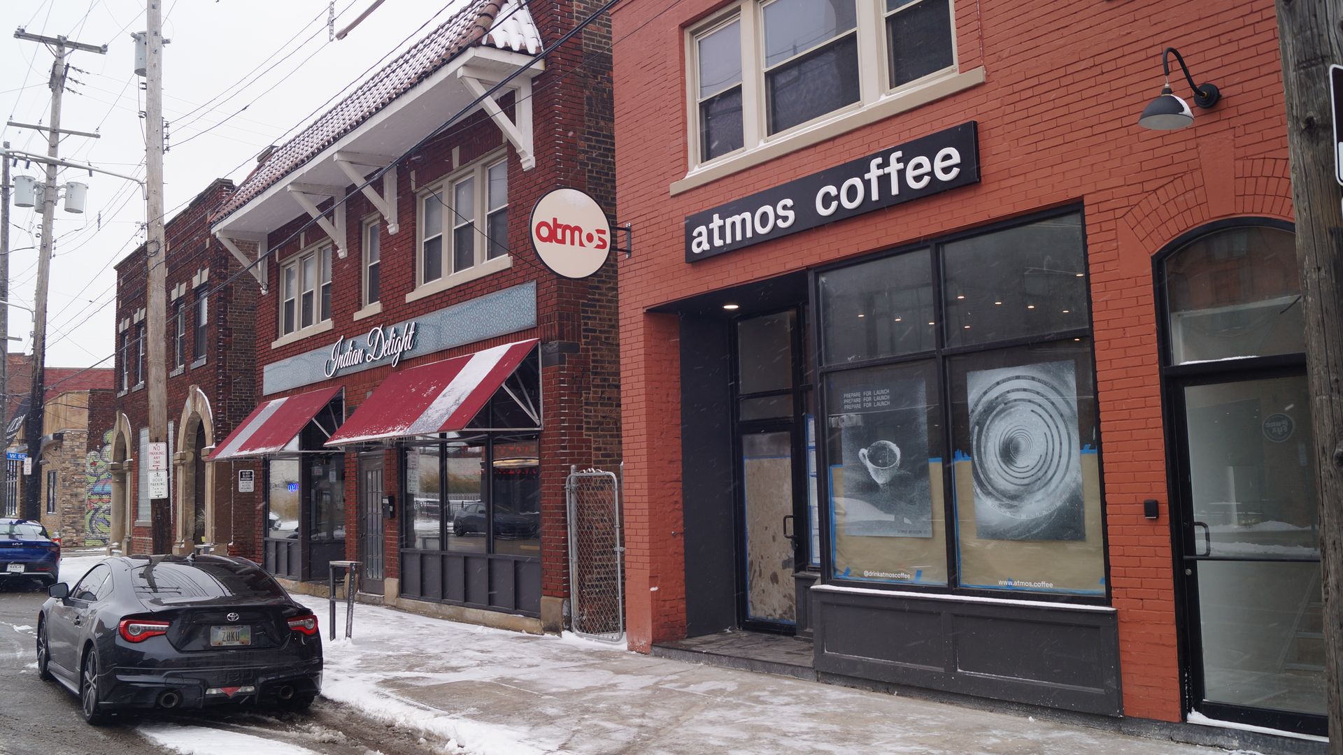 Photo of brick building with glass window and "atmos coffee" signage