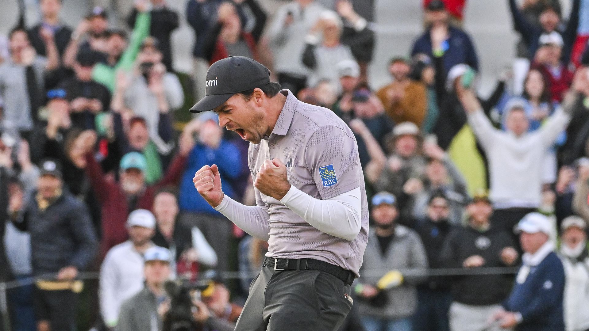 A golfer clenches his fists in front of him and yells victoriously in front of cheering fans. 