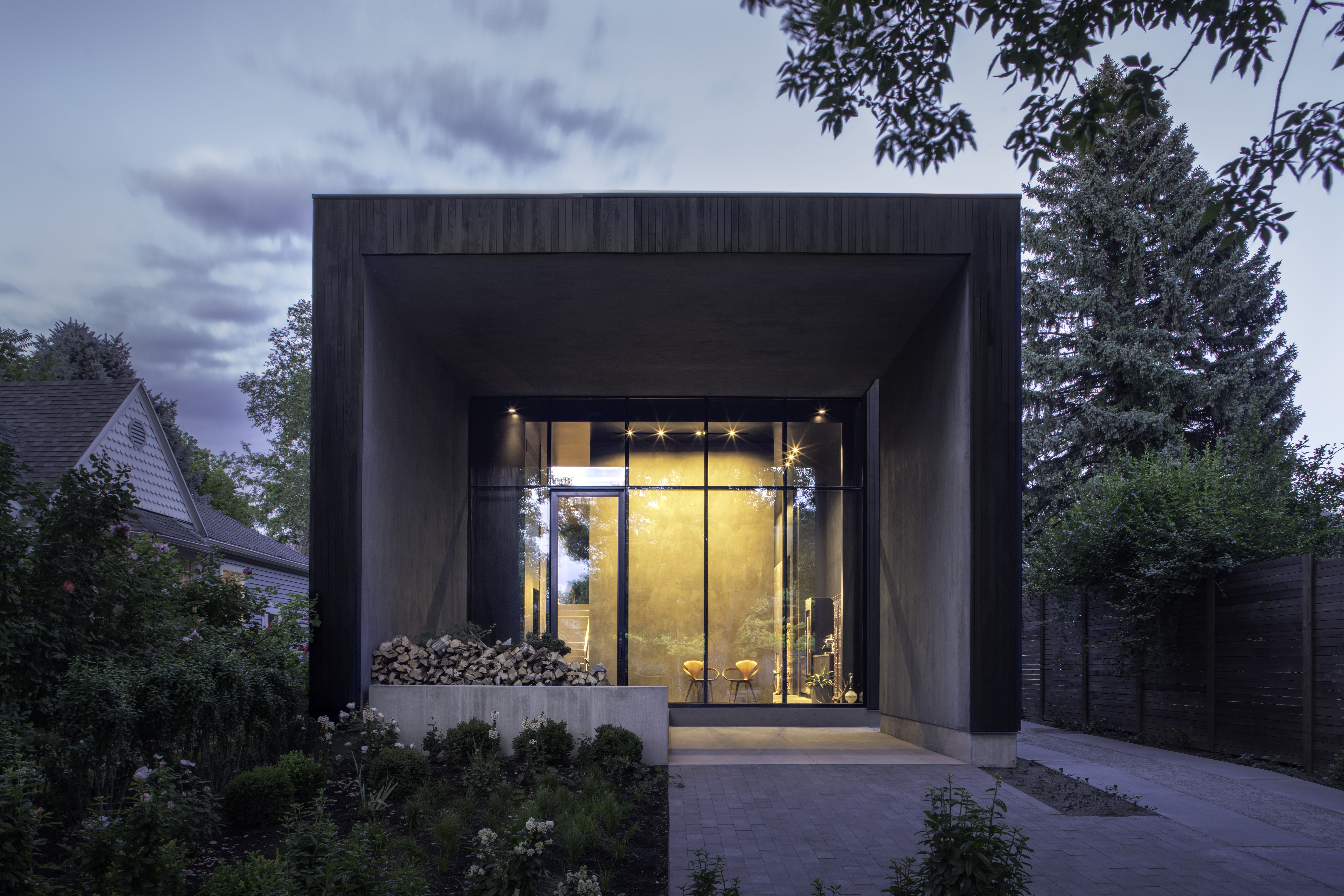 The square exterior of a modern house, with brown siding and a glass wall.