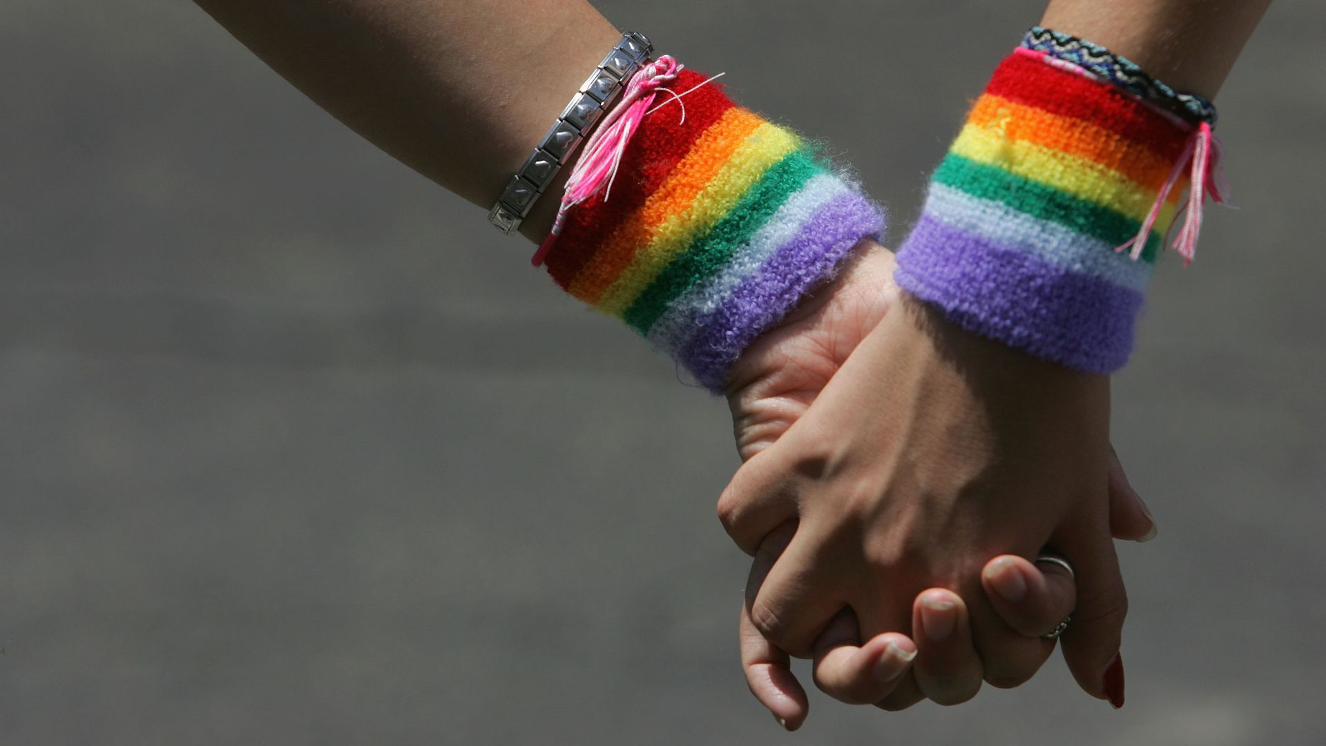 The hands of two women intertwine with pride wristbands on both wrists. 