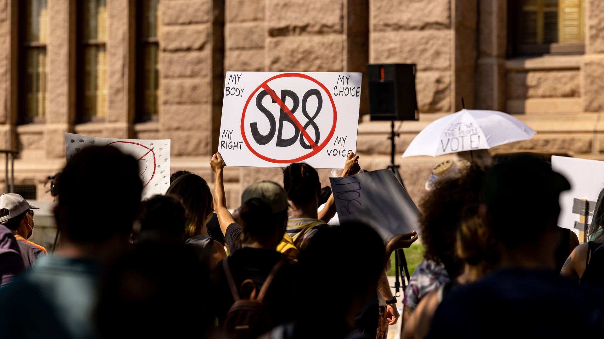 Photo of someone holding a sign that says "SB8" with a red X drawn over it
