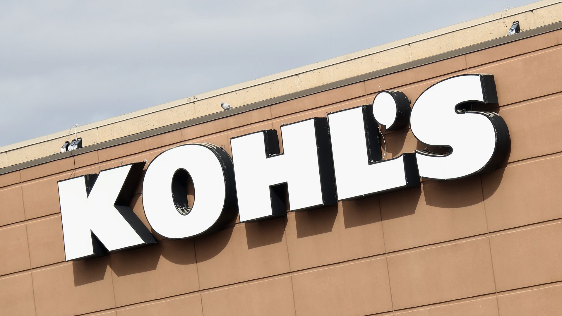 Signage spelling out the Kohl's name in white lettering appears on the side of a tan-colored building.