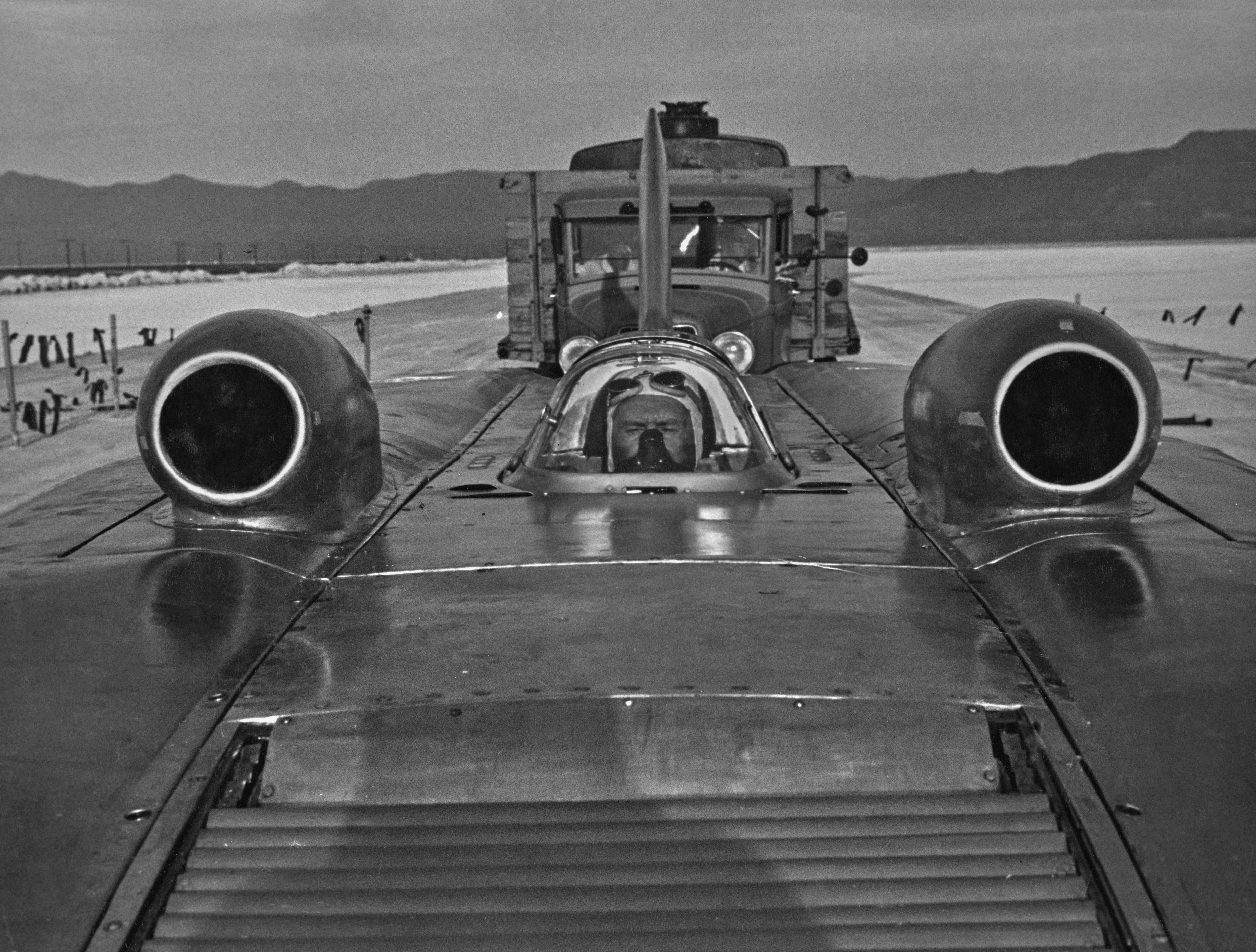 A man in a race car wears a gas mask to avoid inhaling fumes.