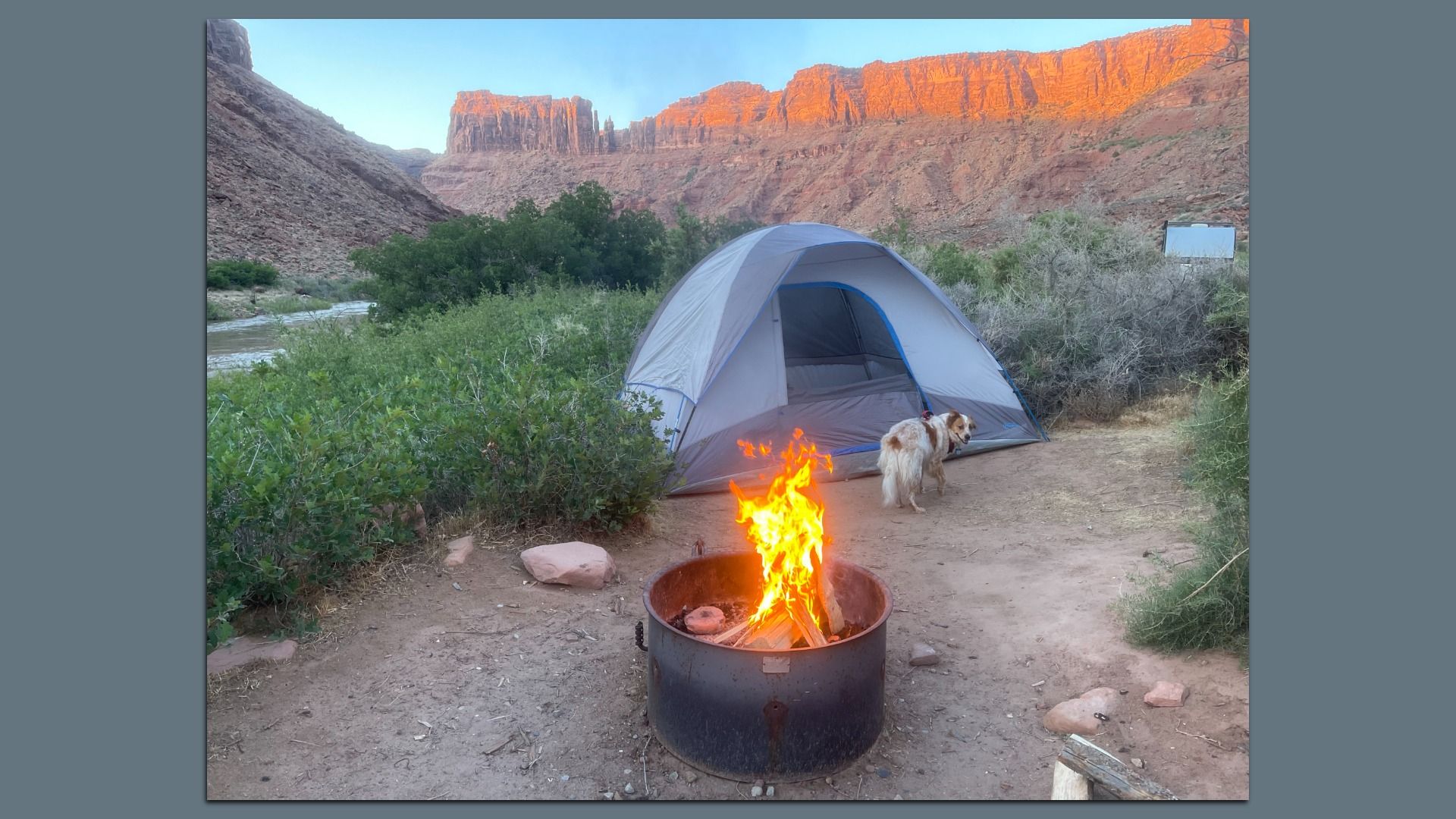 A campfire in front of a tent with scenic hills in the background