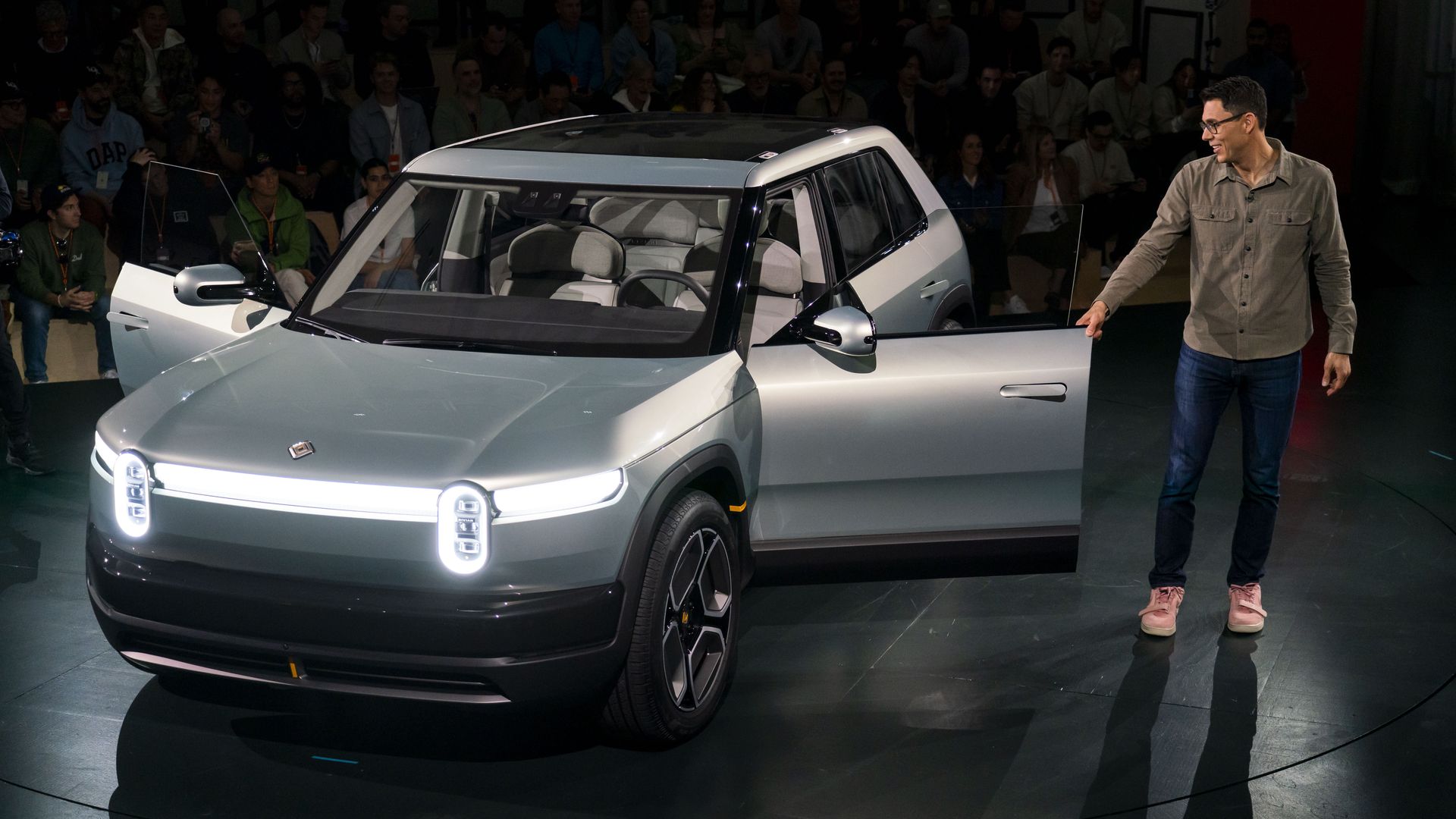 A man stands next to a gray silver sleek midsize SUV at a publicity event