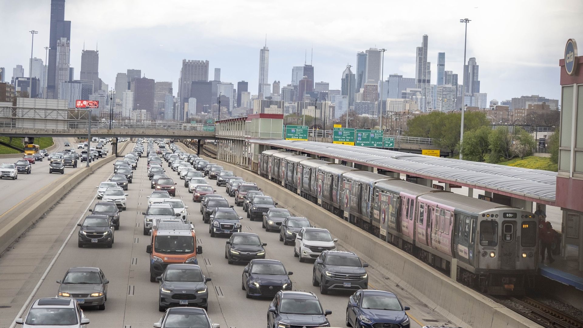 Photo of traffic next to a train going away from a downtown 