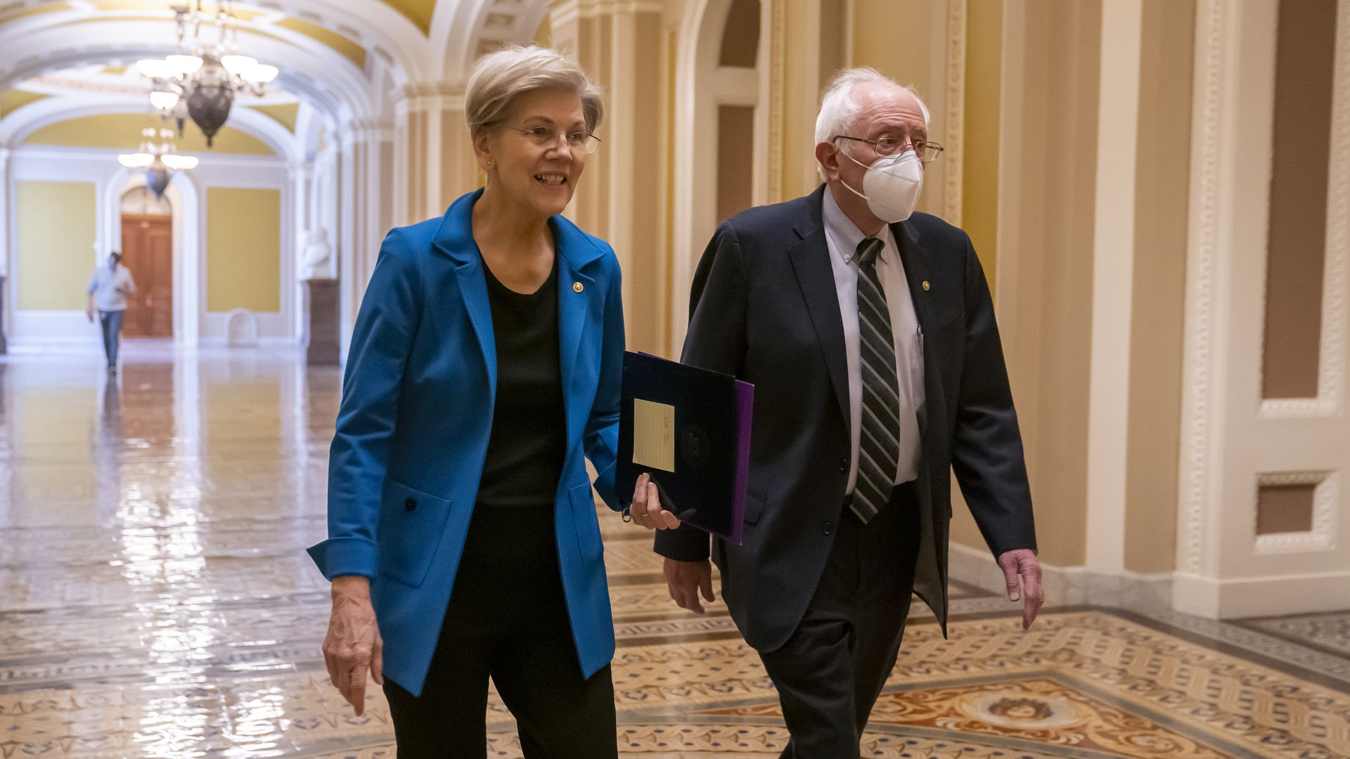 Elizabeth Warren and Bernie Sanders walk down a hall in the Capitol