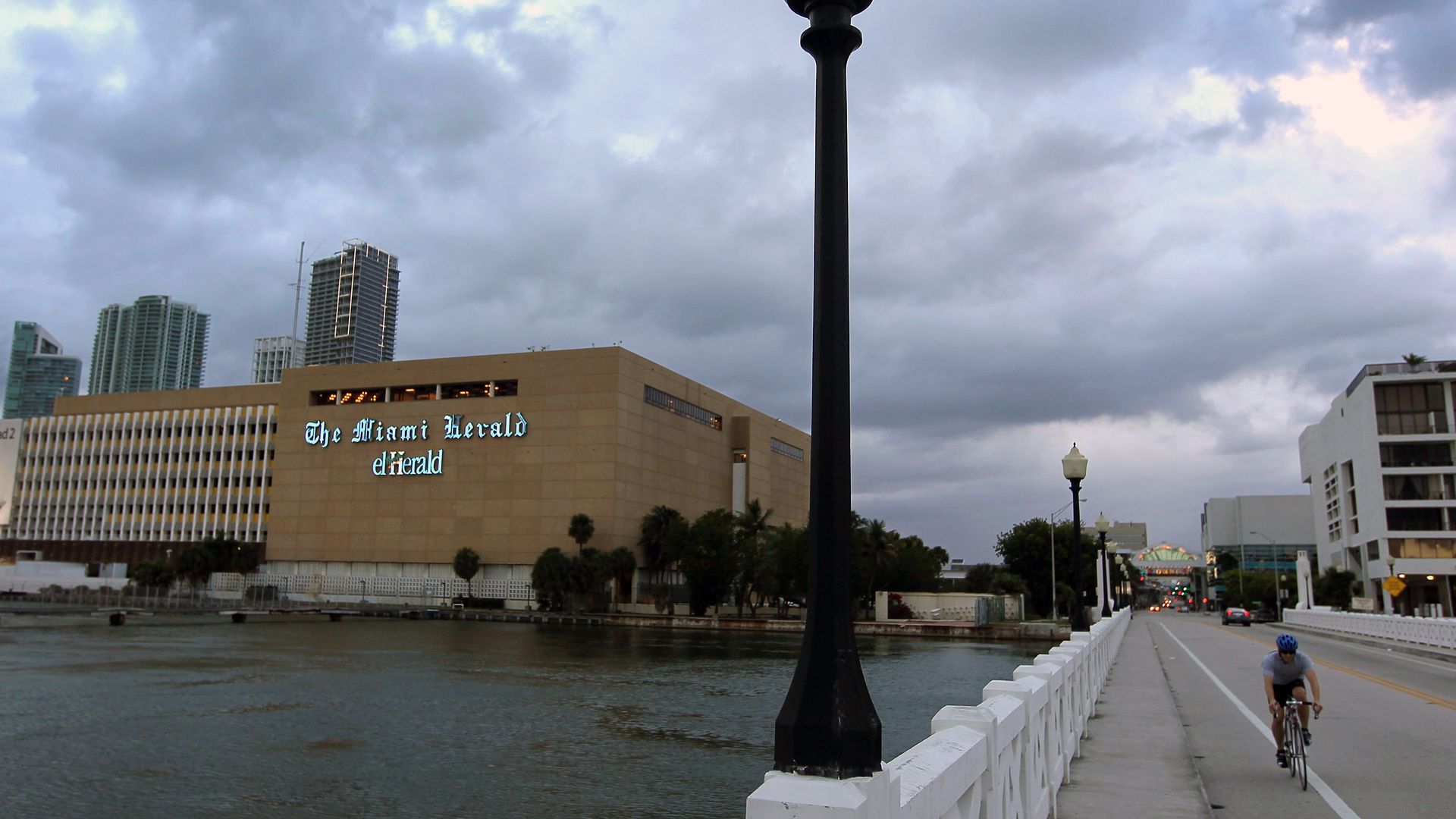 A large boxy building that says Miami Herald beside the water and a bridge