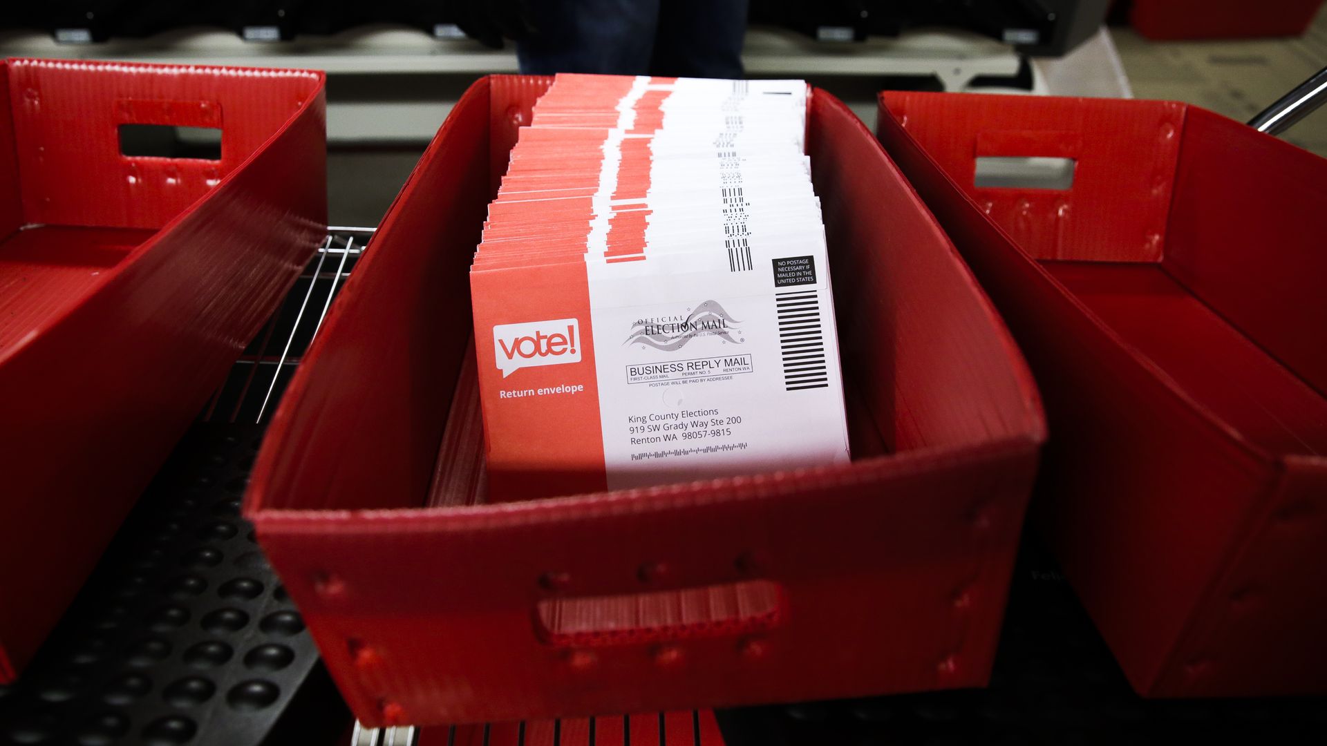 An up close photo of a red basket filled with red and white mail-in ballots.