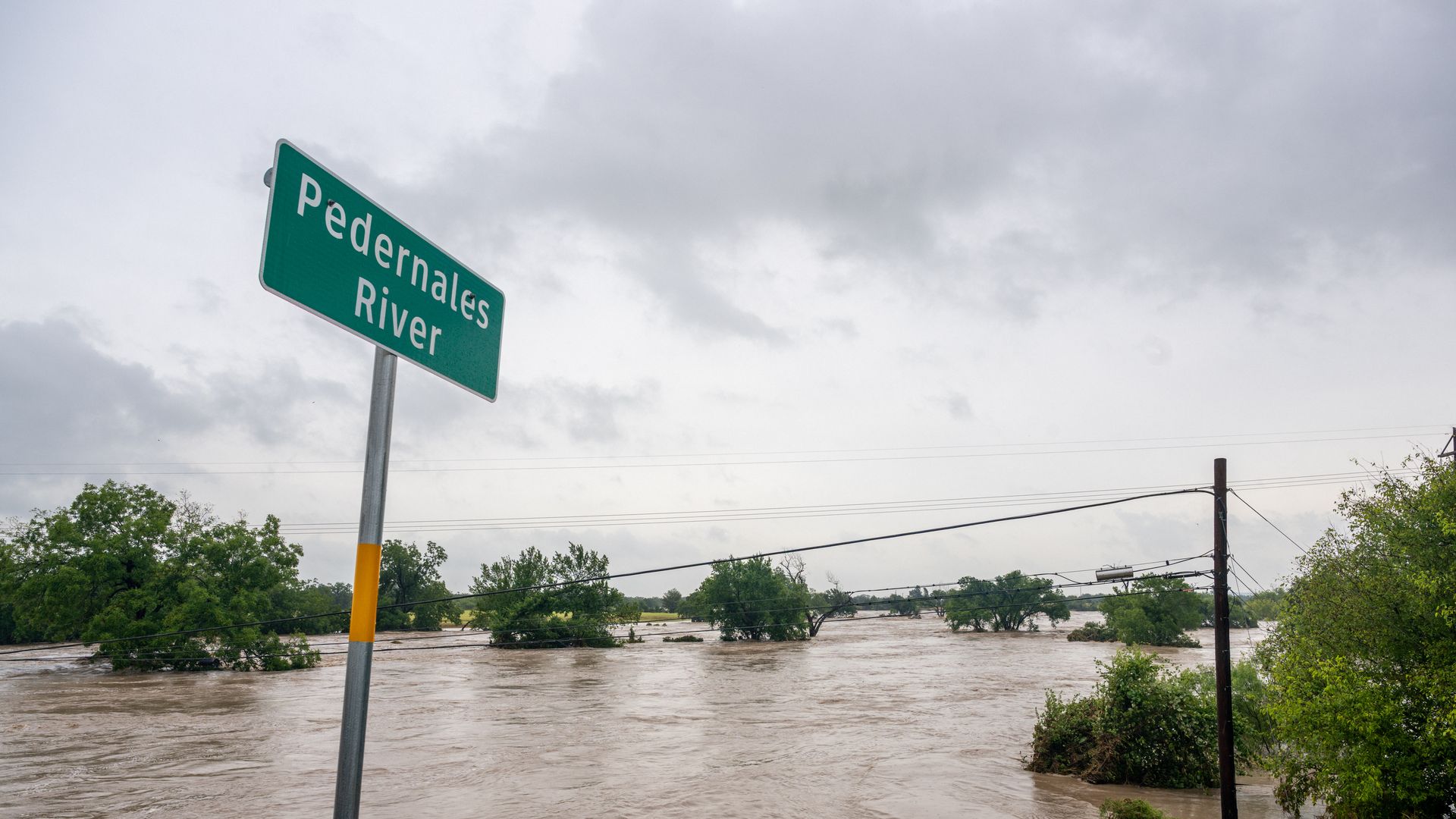 High rising brown water is shown along a green sign that says "Pedernales River" near Austin, Texas
