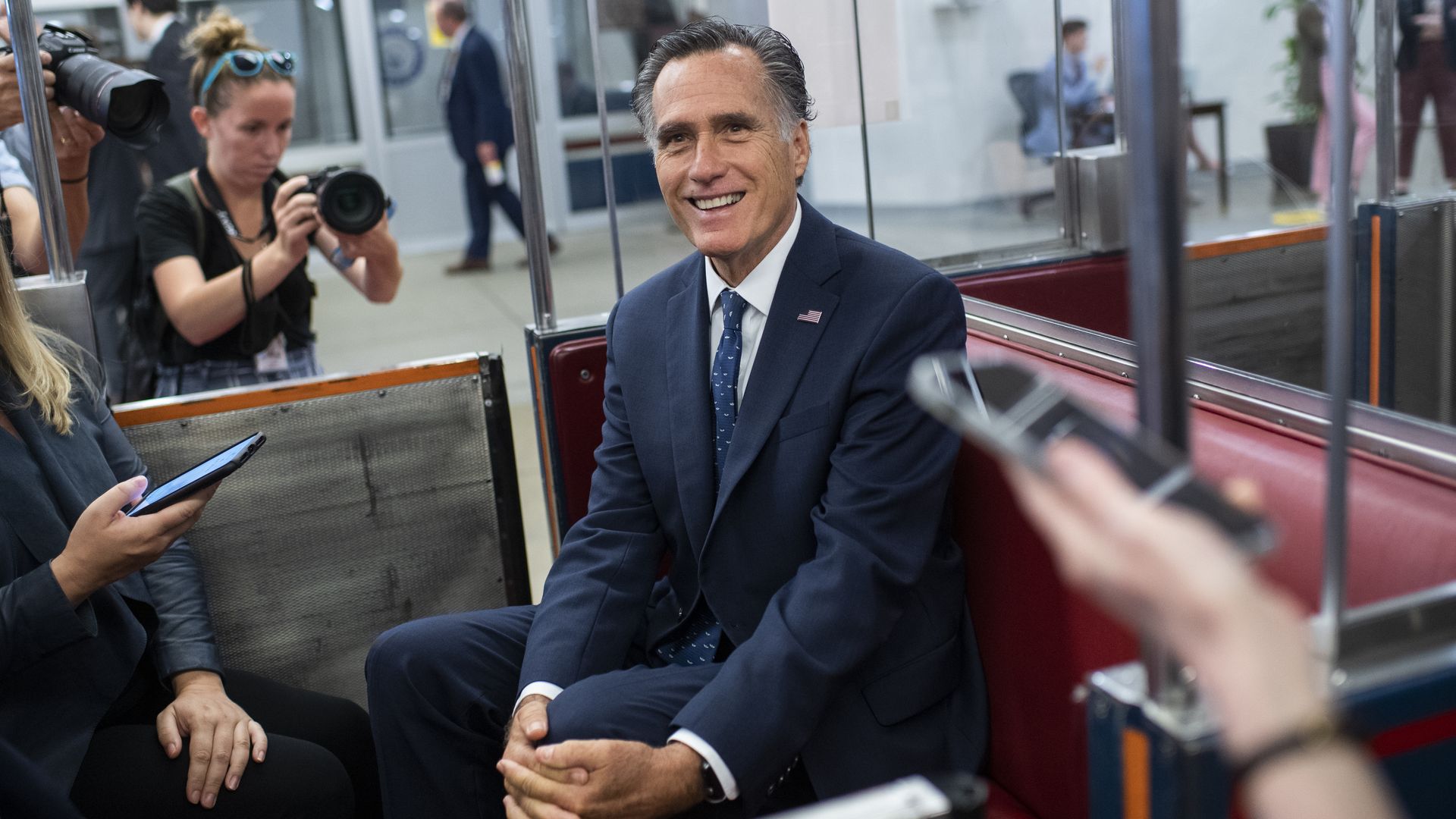 Sen. Mitt Romney is seen smiling as he sits in a Senate subway car as he discusses infrastructure negotiations.