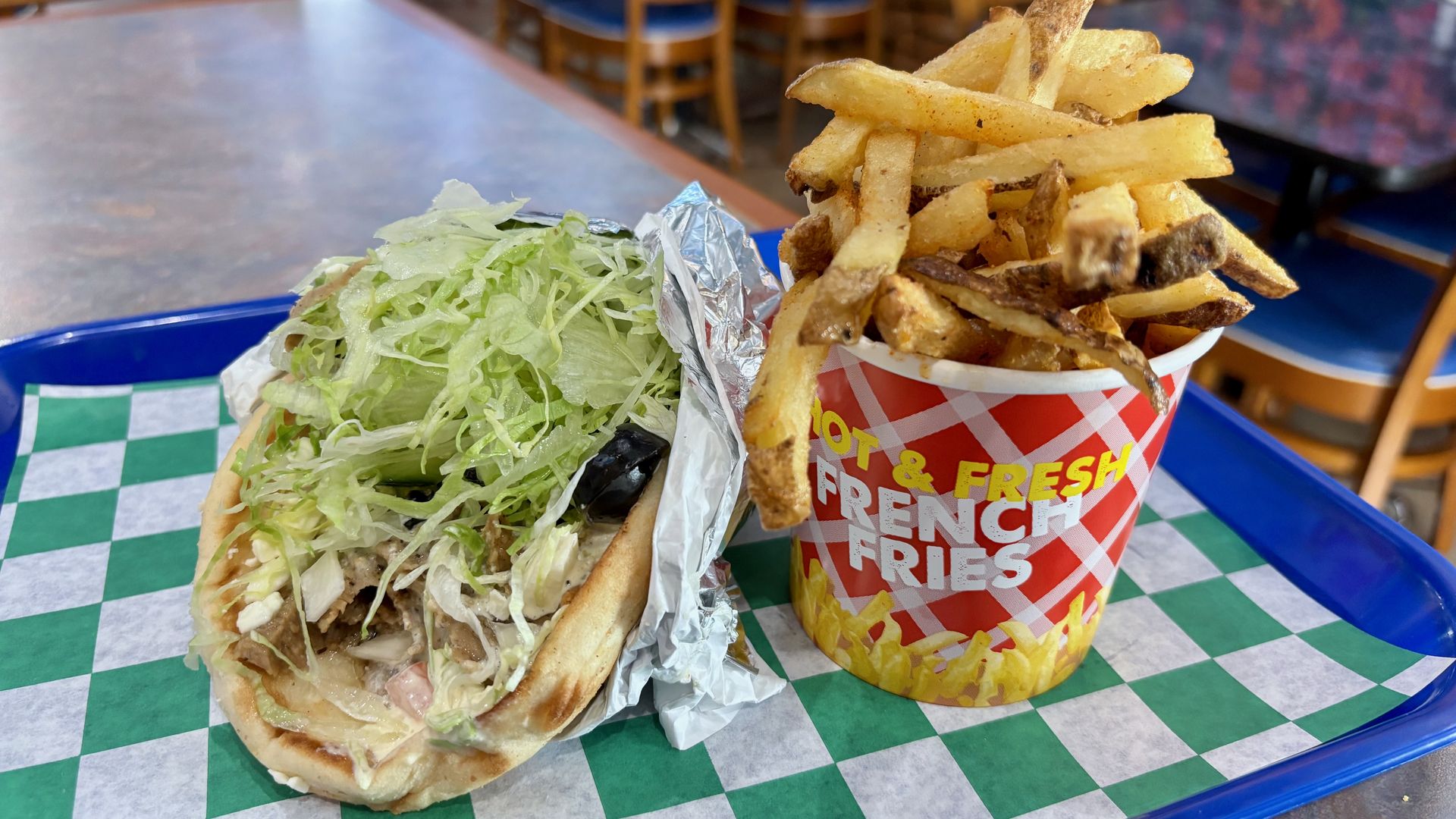 A gyro wrapped in foil, topped with lettuce, and a towering cup of fries on a food tray