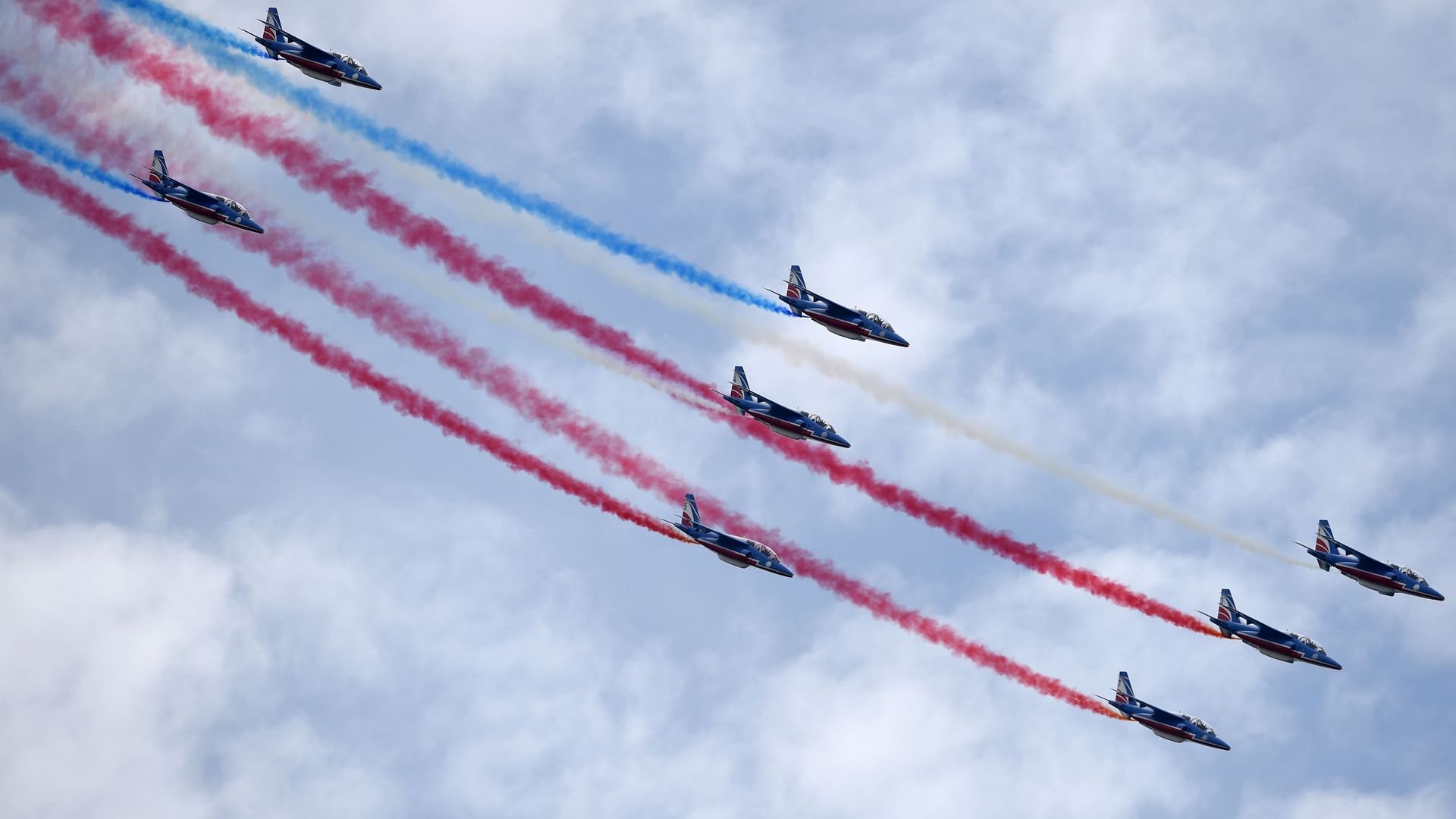 Eight acrobatic aircraft fly in sync, shooting red, blue and white smoke out the back. 
