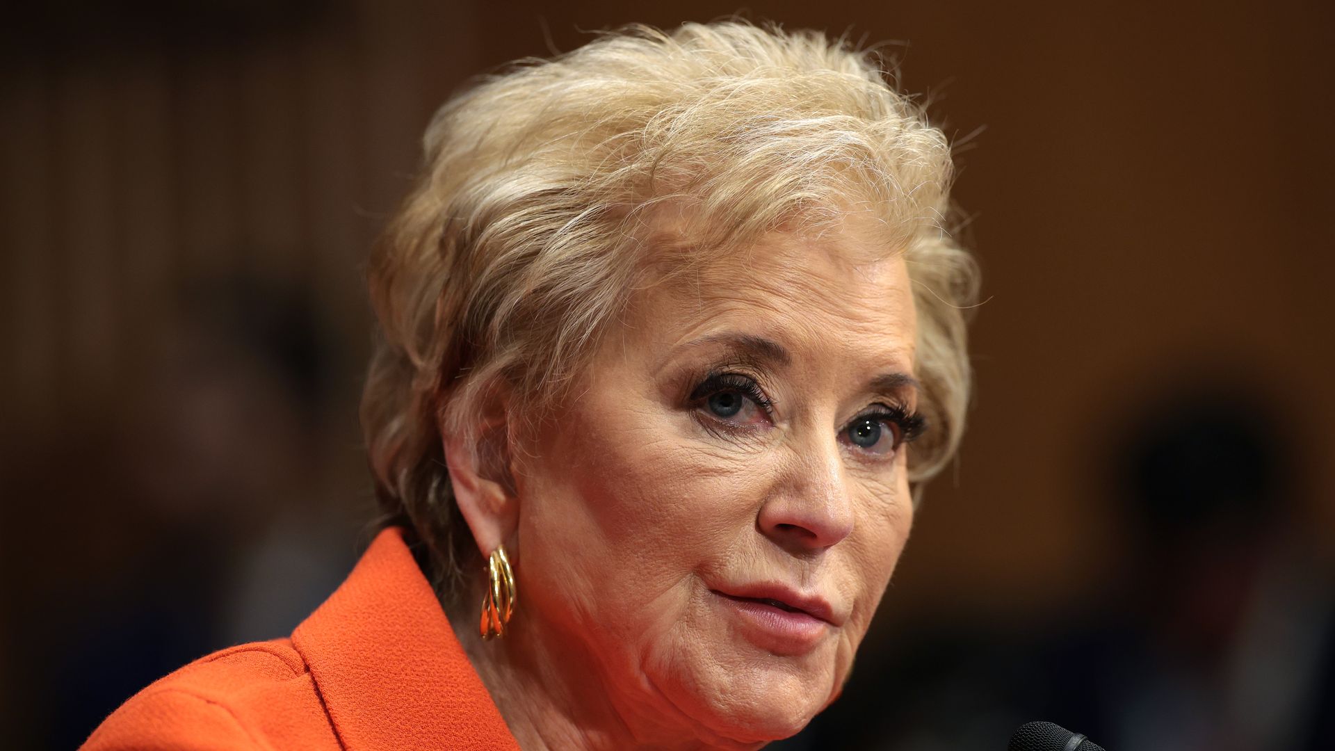 Linda McMahon looks to the side and speaks into a microphone as she testifies on Capitol Hill.
