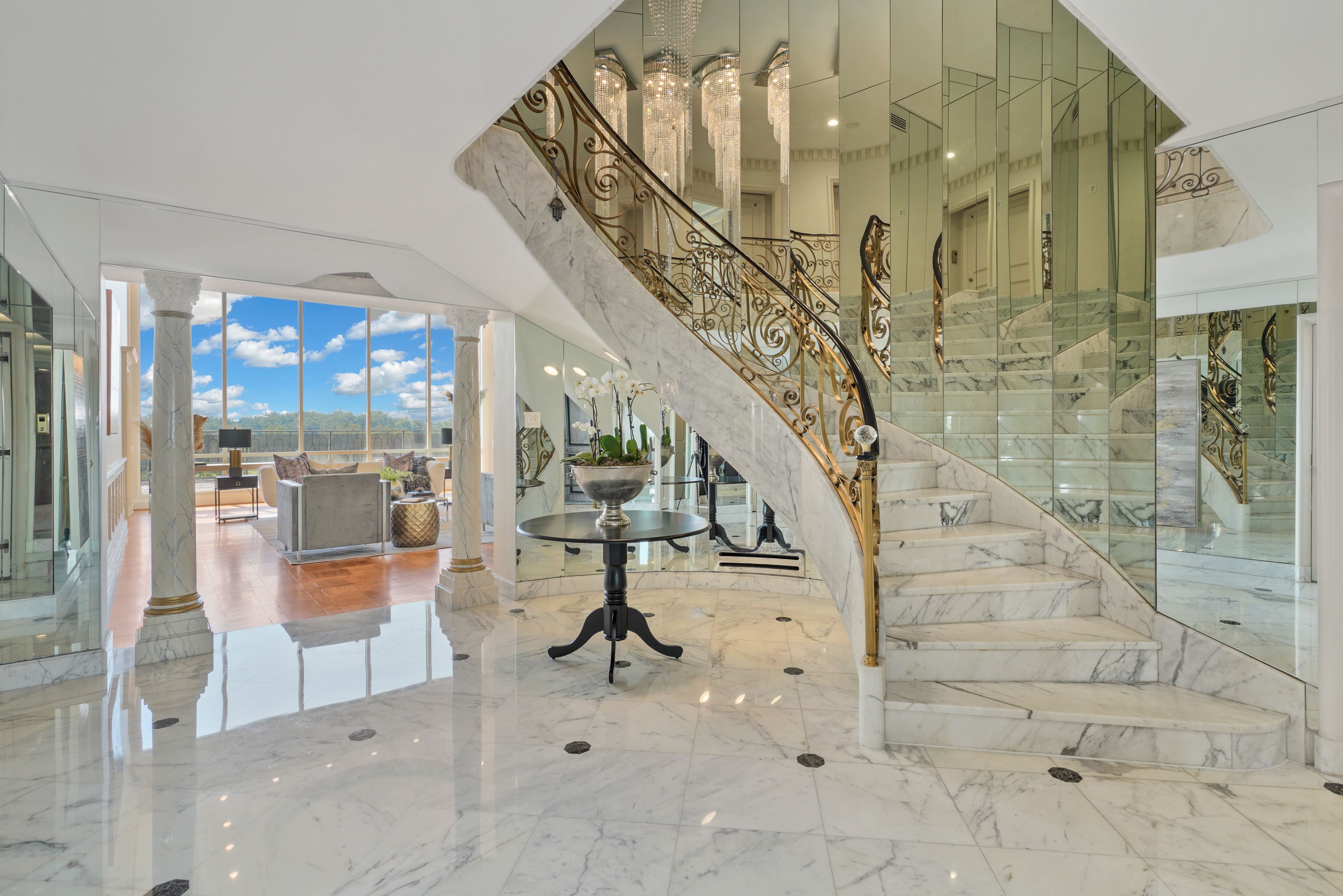A marble foyer with a marble and gold stairway in a luxury condo.