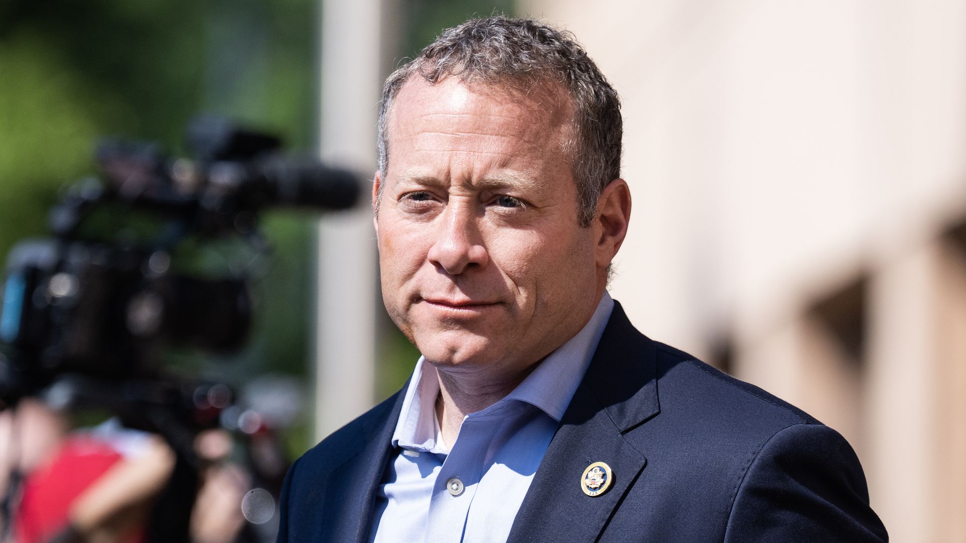Rep. Josh Gottheimer, wearing a blue suit and standing next to a TV camera in front of a beige building.
