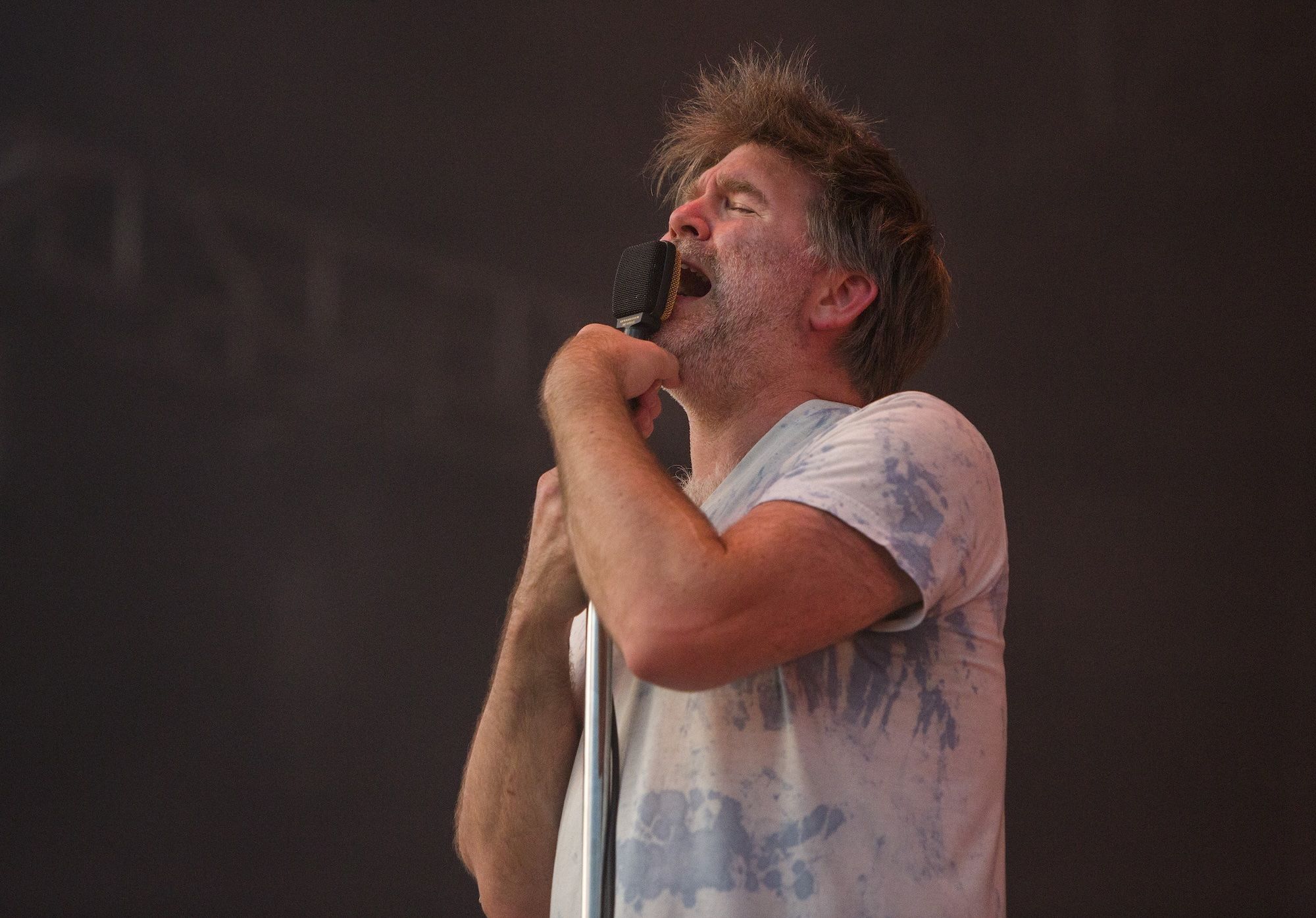 James Murphy in t-shirt holding a microphone close with his eyes closed.