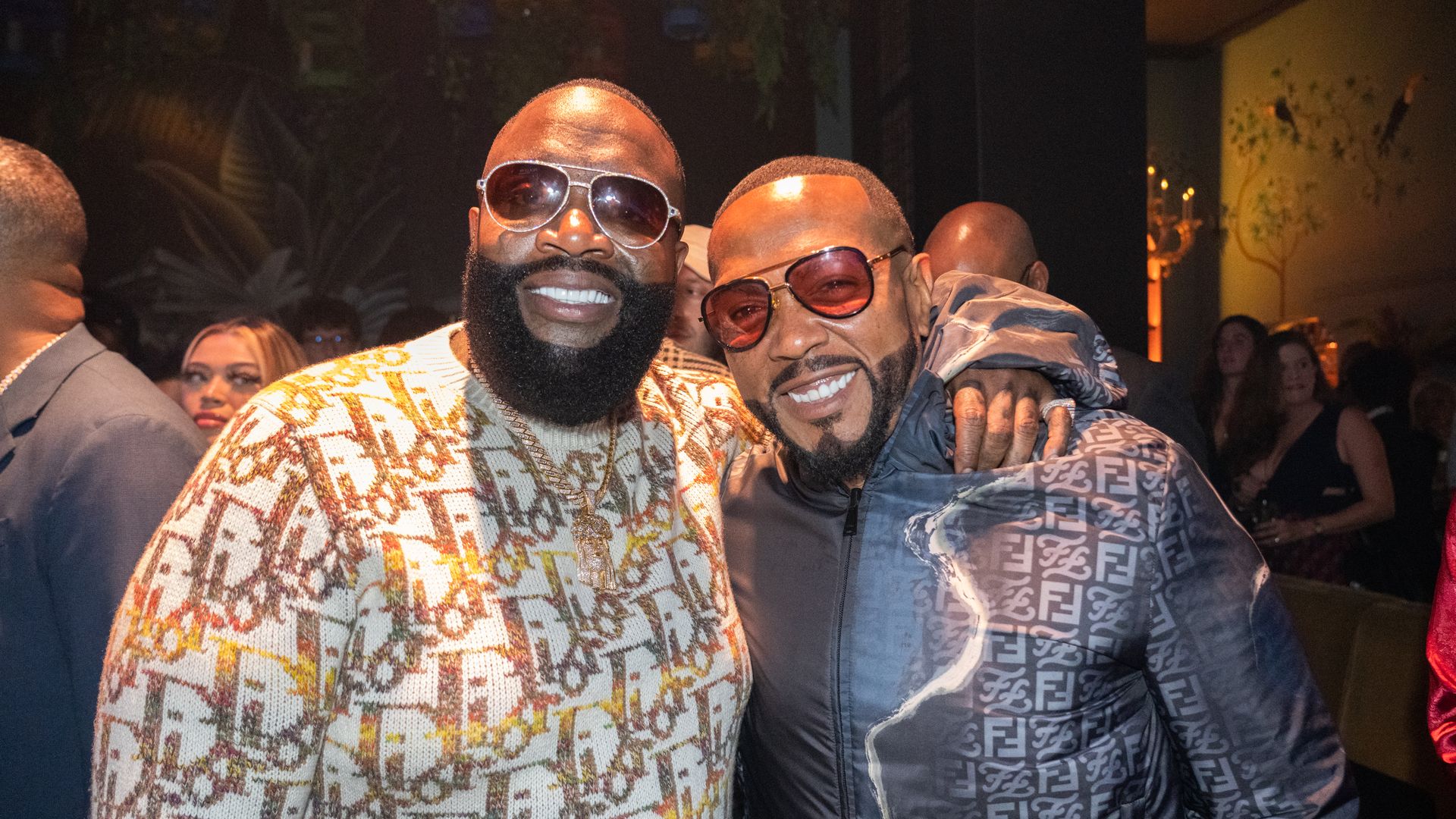 Rapper Rick Ross puts his arm around Timbaland as both men smile and wear sunglasses. 