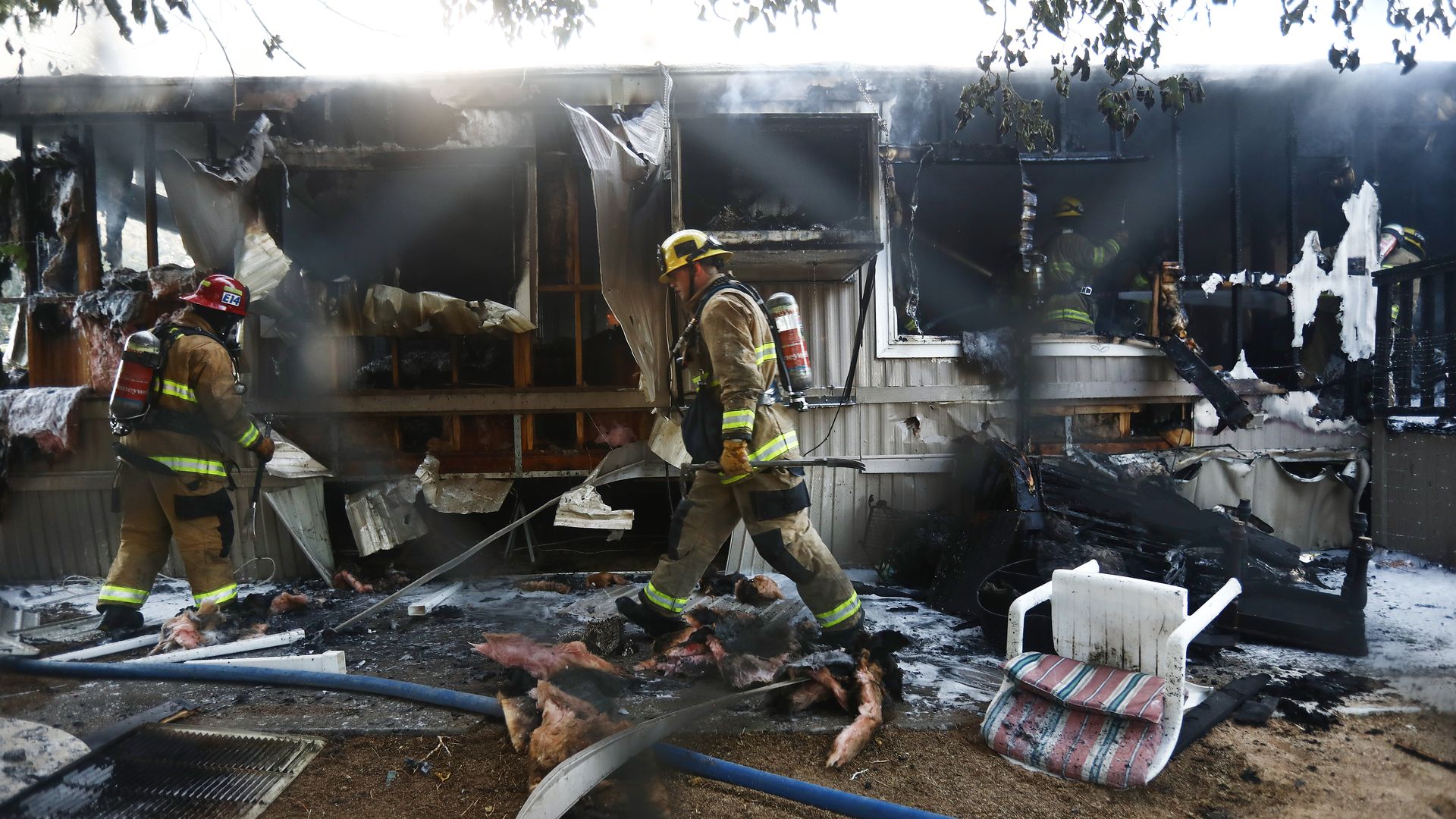 In this image, firefighters walk through the rubble of a mobile home.