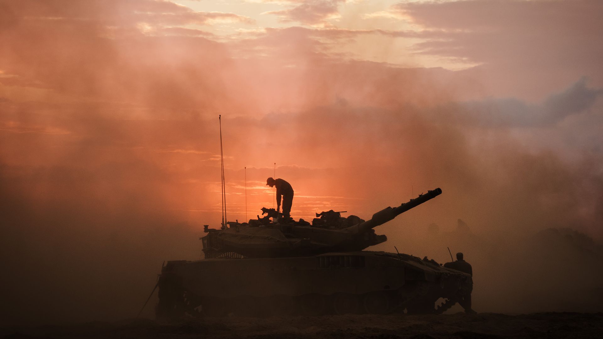 A soldier stands on a tank sillouhetted against a red sky. 