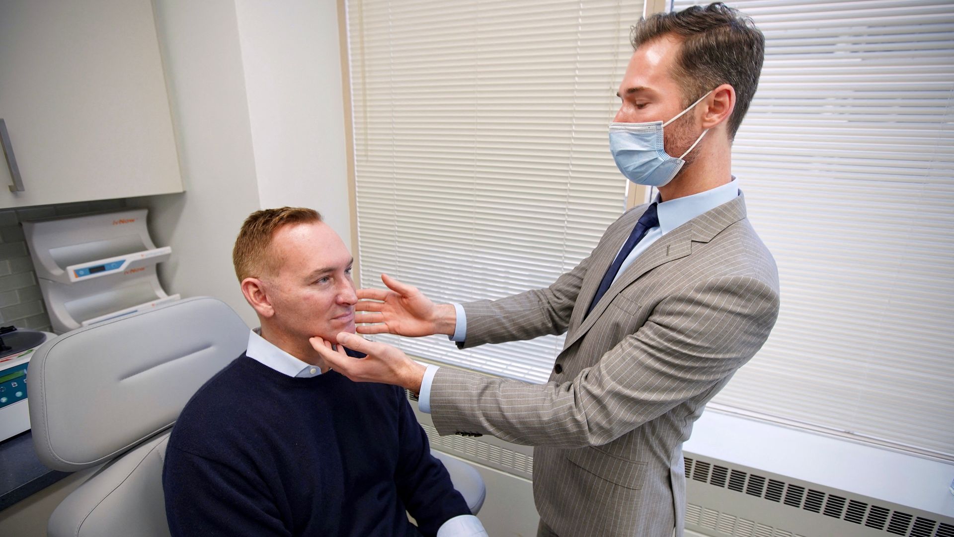 A plastic surgeon examines a male patient in a doctor's chair.
