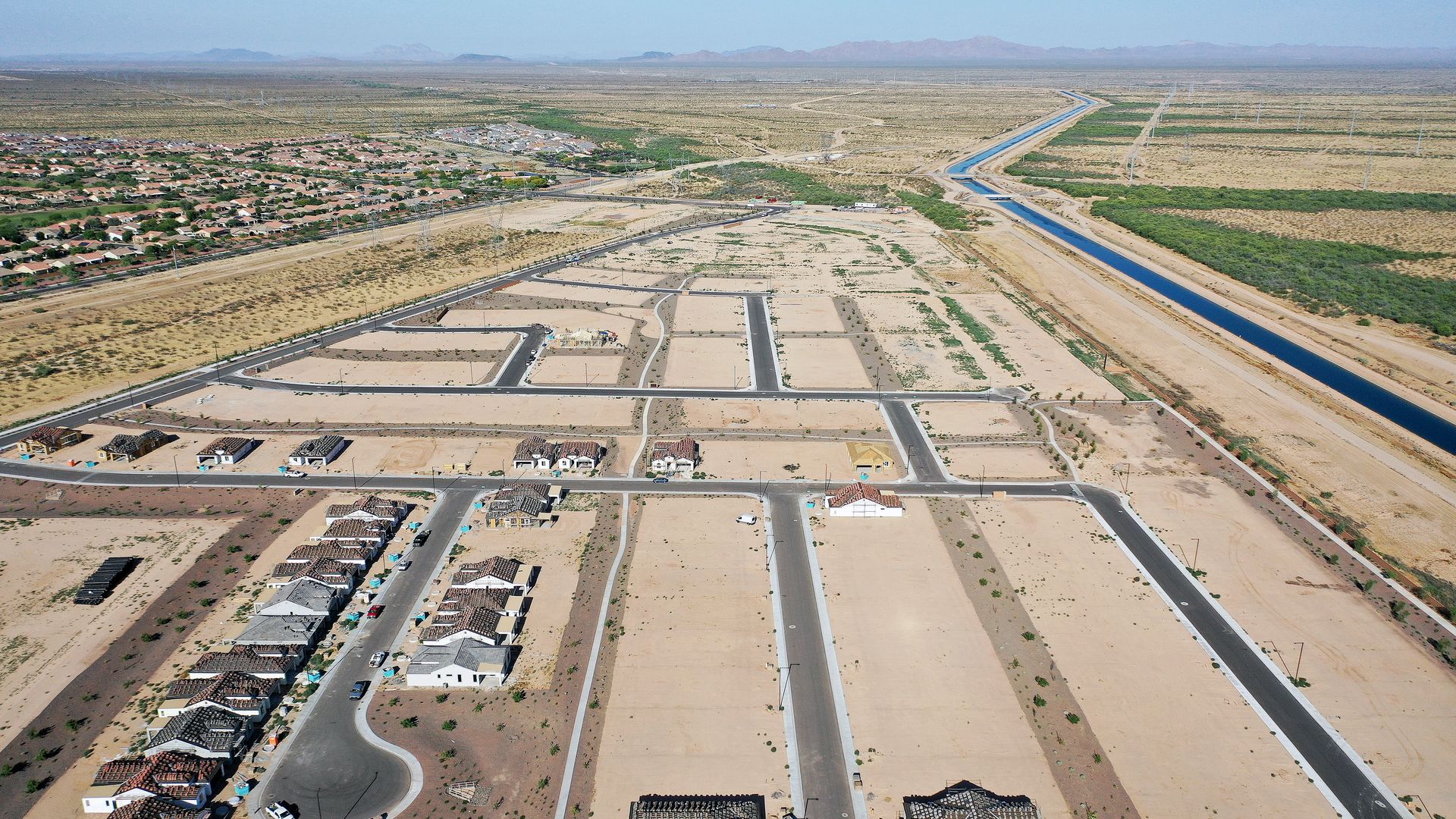 Aerial view of a partially built housing subdivision in the desert with a canal running alongside it.