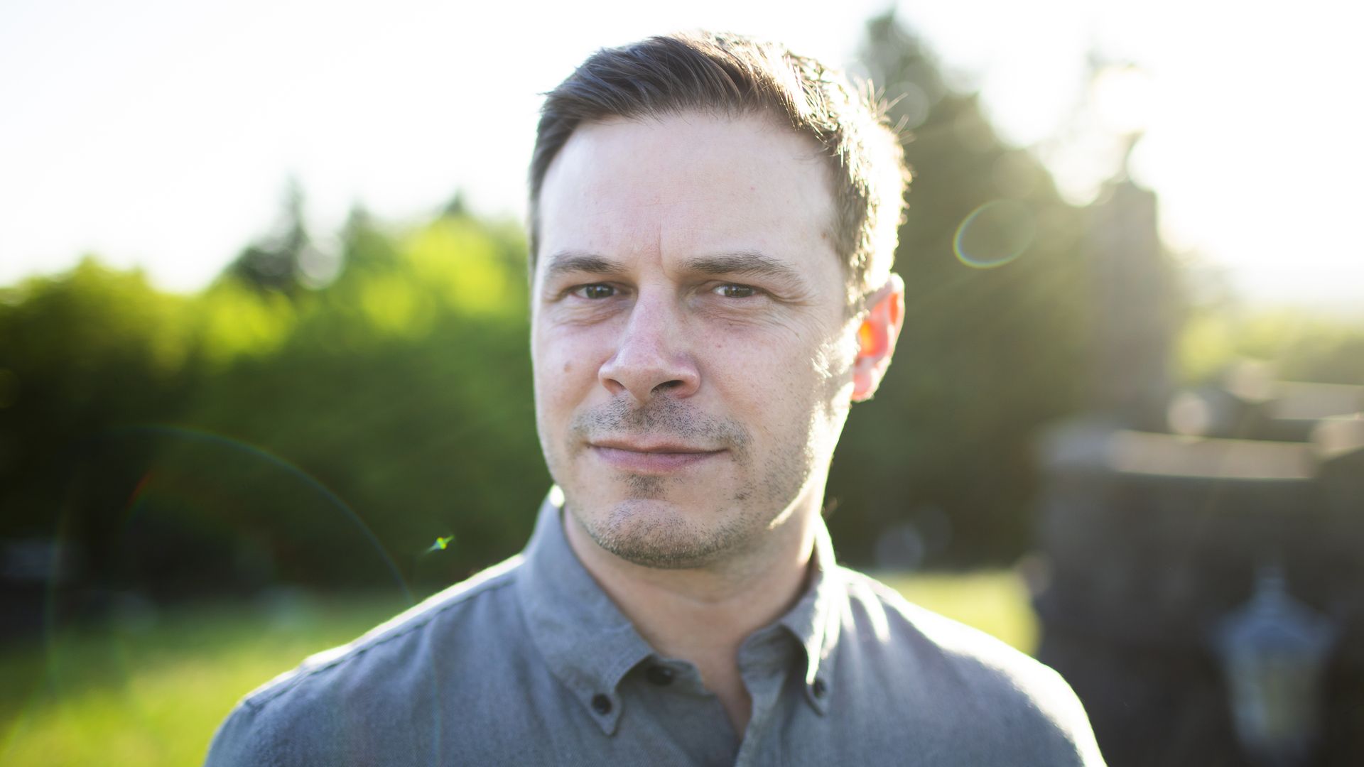 Writer Kale Williams poses for a portraIt with trees in the background.