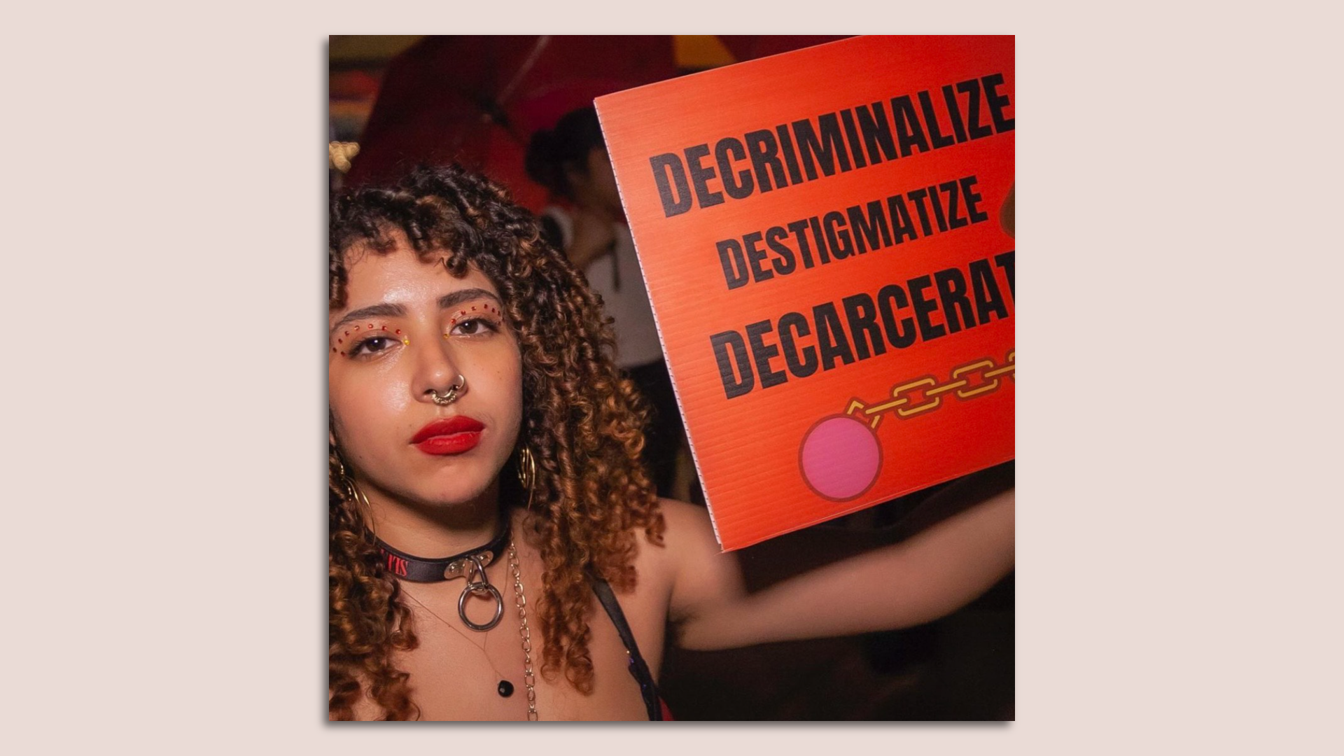 A woman with red lipstick holds up a red sign that says "Decriminalize, destigmatize, decarcerate."