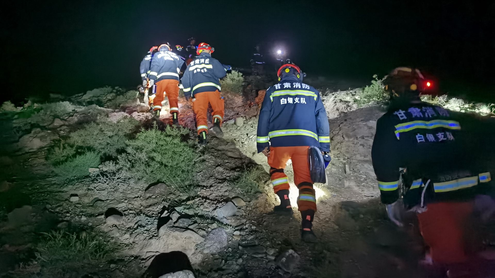 A line of emergency responders walk up a hiking trail at night
