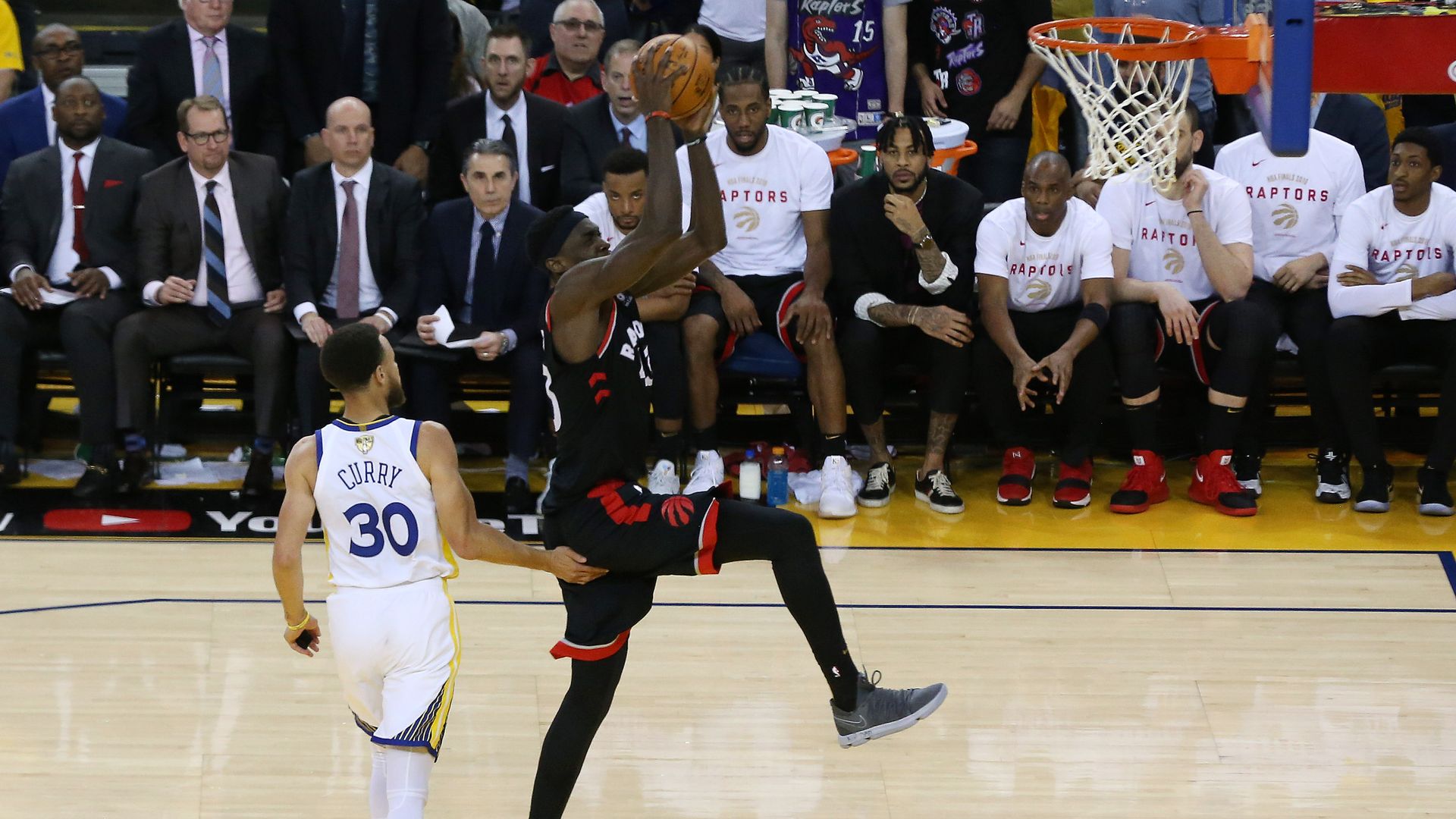 In this image, one player dunks a ball while another stands nearby.