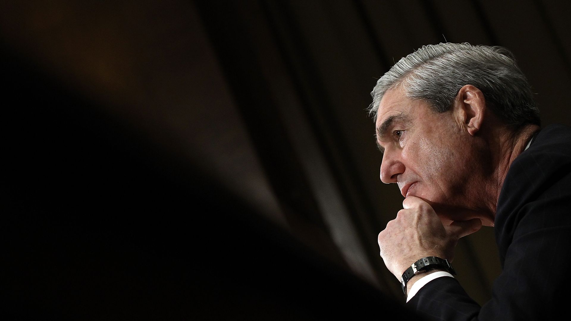 In this image, Robert Mueller looks to the left while resting his chin on his hand. 