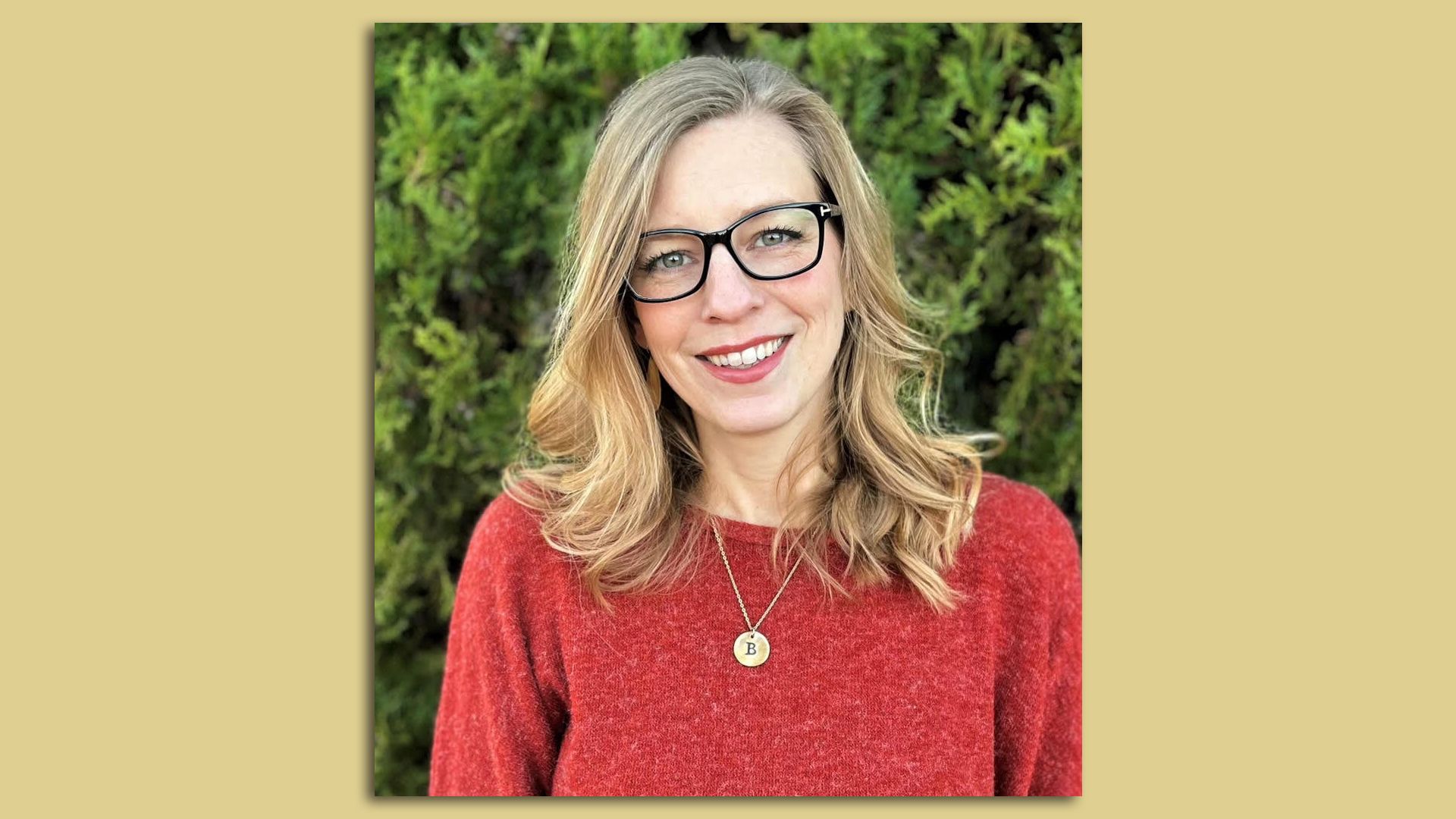 A photo of a woman wearing glasses, standing in front of a green tree.