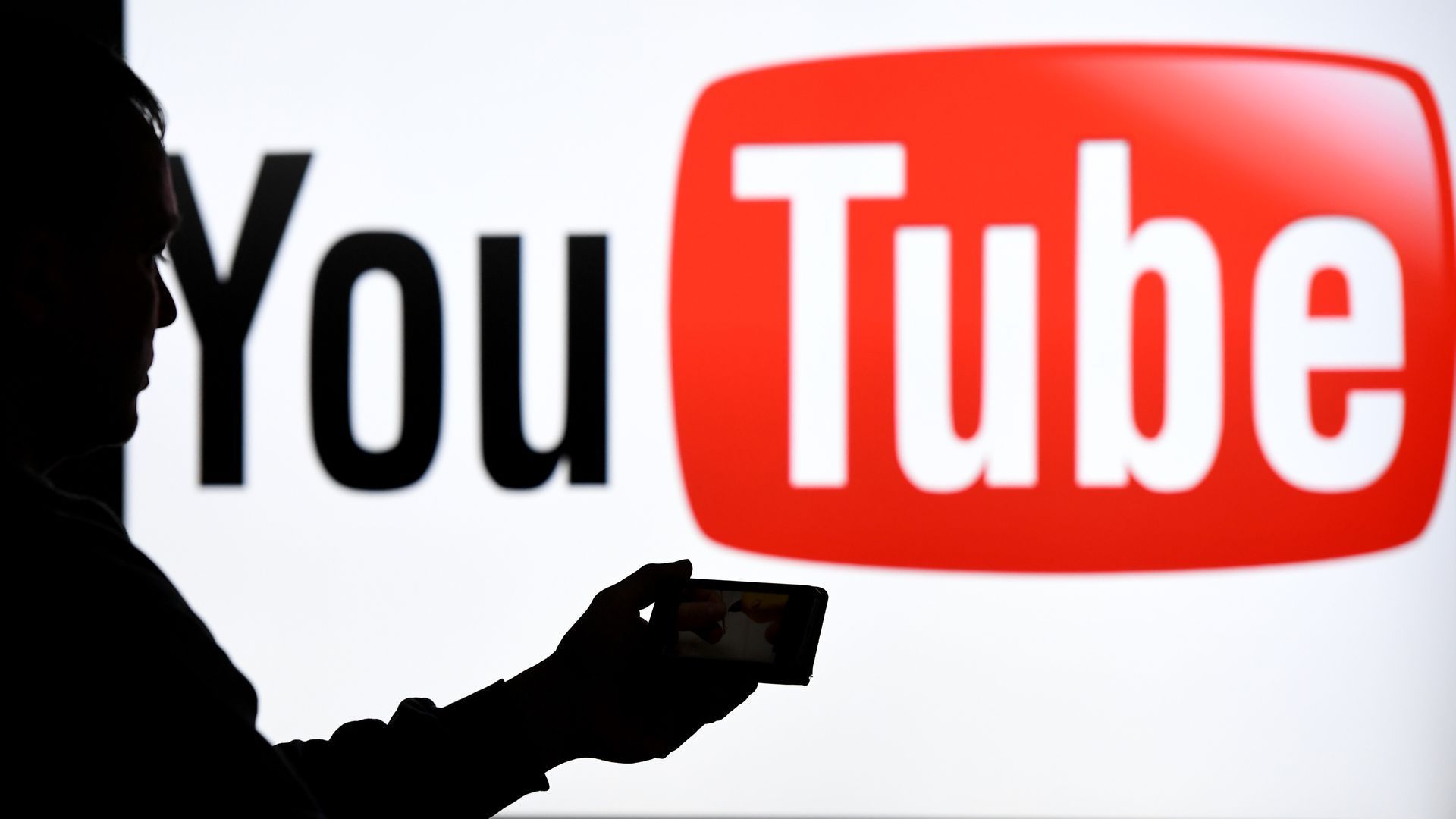 A photo illustration of a smartphone user in shadow against YouTube logo background