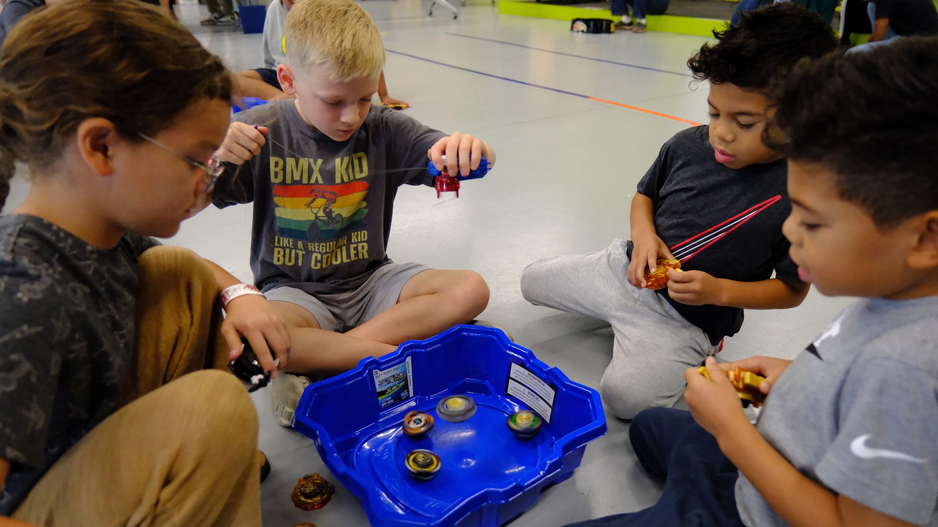 Four children sitting around a small Beyblading stadium