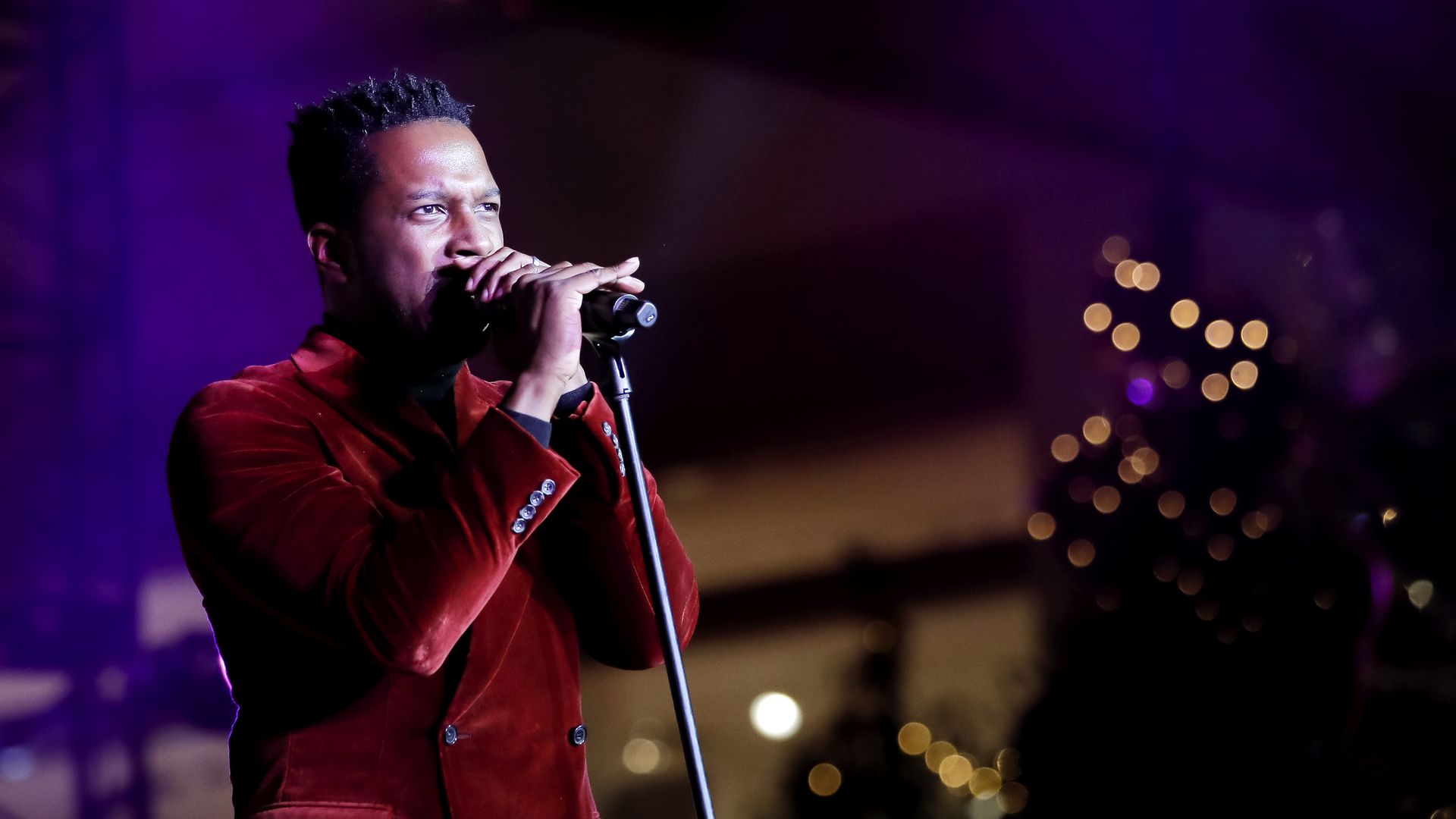 Photo of Leslie Odom Jr. in a red seat singing into a microphone