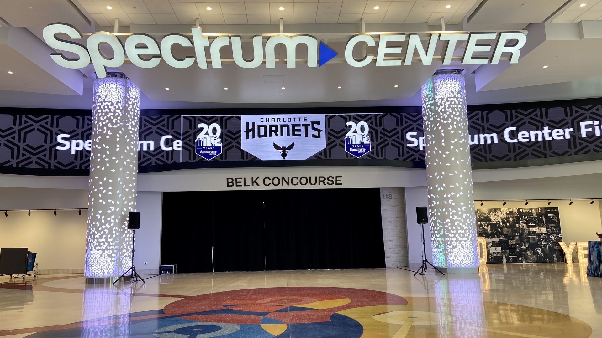 Entrance to Spectrum Center's Belk Concourse, with illuminated pillars, a large sign celebrating 20 years of Spectrum Center, and Charlotte Hornets logo above.