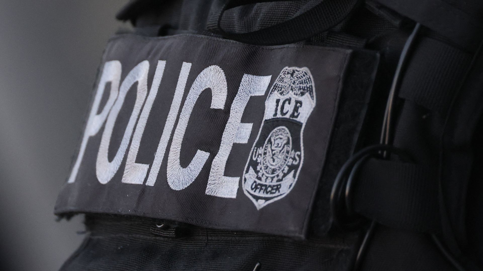 A close-up of a rectangular, black patch with the word "Police" next to a law enforcement badge with the words "ICE Officer" on the front of a black uniform. 