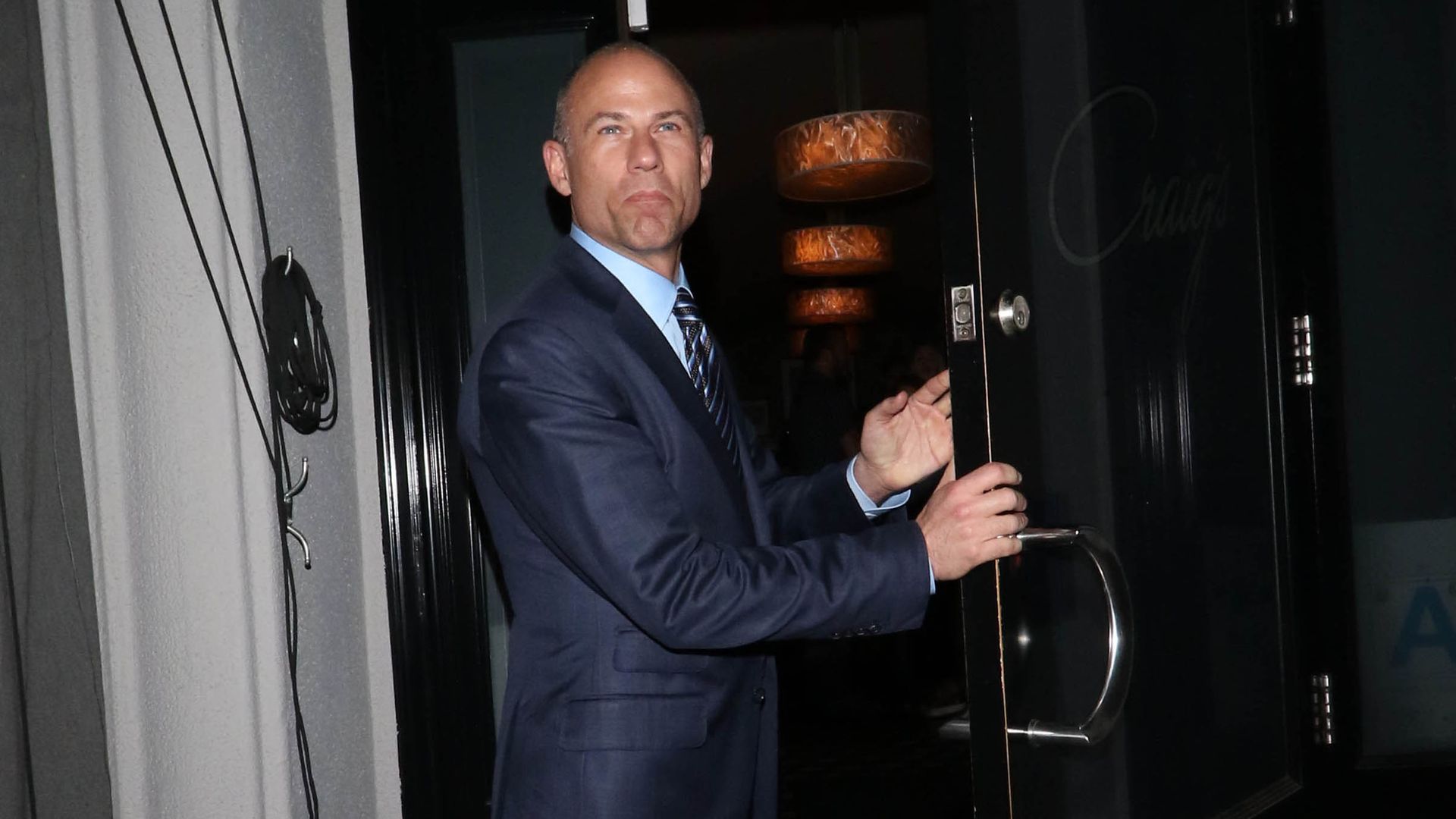Michael Avenatti stands in a doorway holding a door open