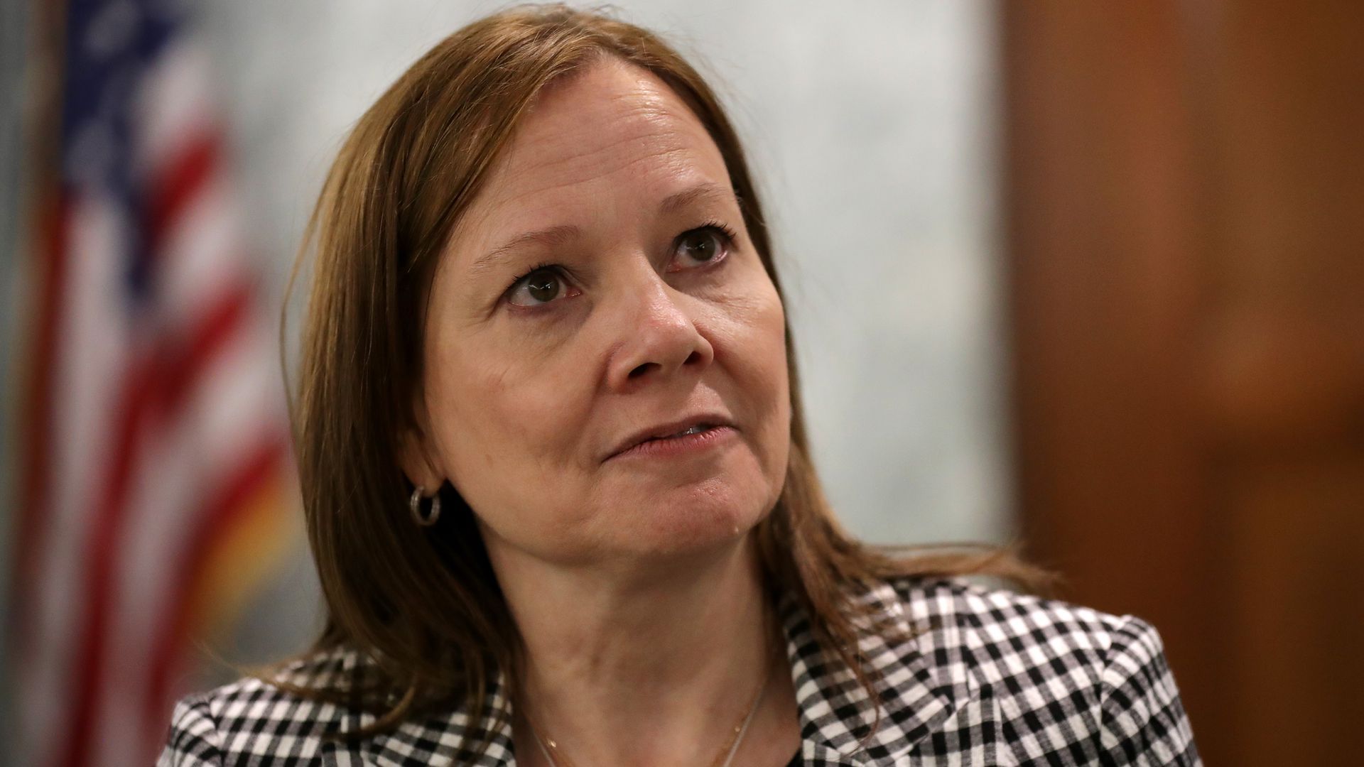 GM CEO Mary Barra stands wearing a plaid checkered suit jacket