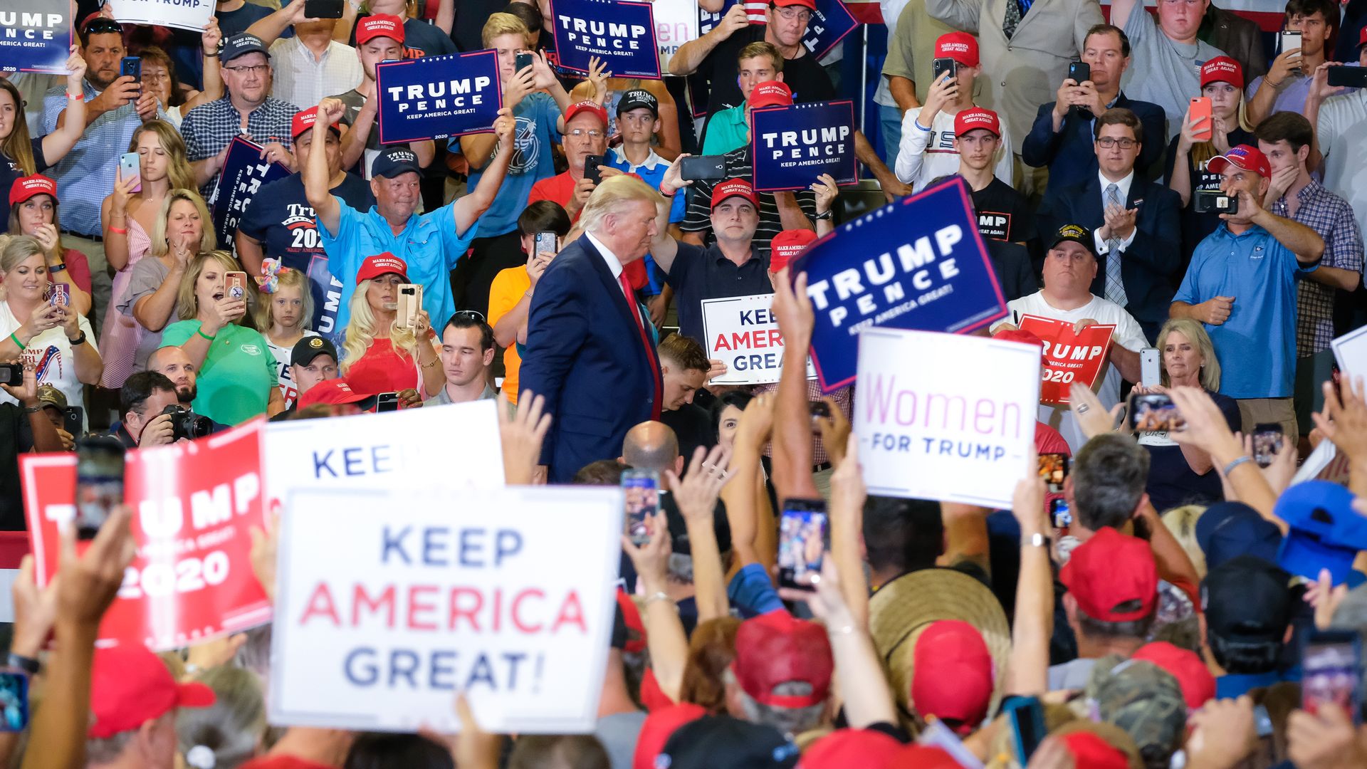 Trump walks through a crowd holding Trump Pence signs at a rally.