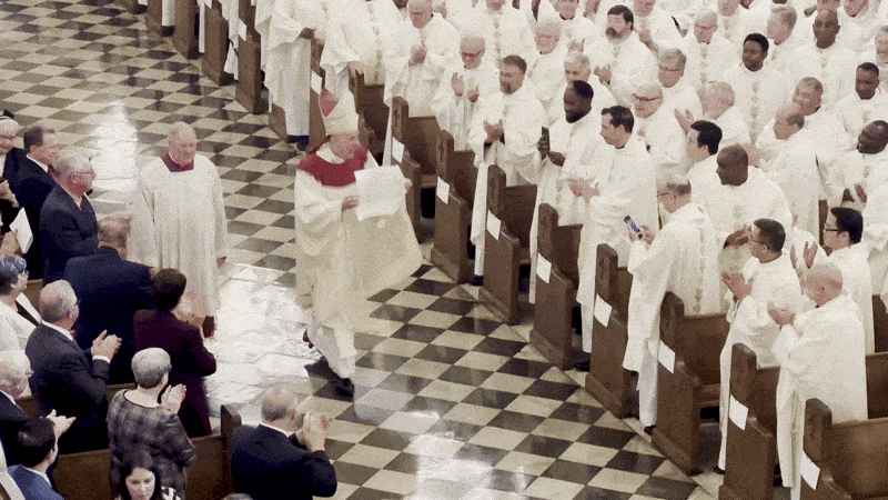 Image shows Archbishop Checchio wearing white robes and displaying a mandate in a church.