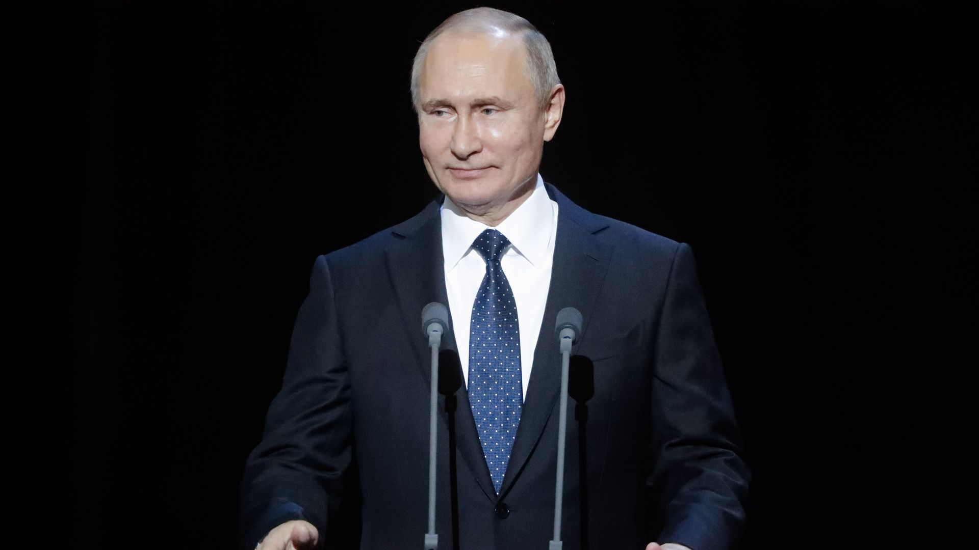 Vladimir Putin at podium smiling.