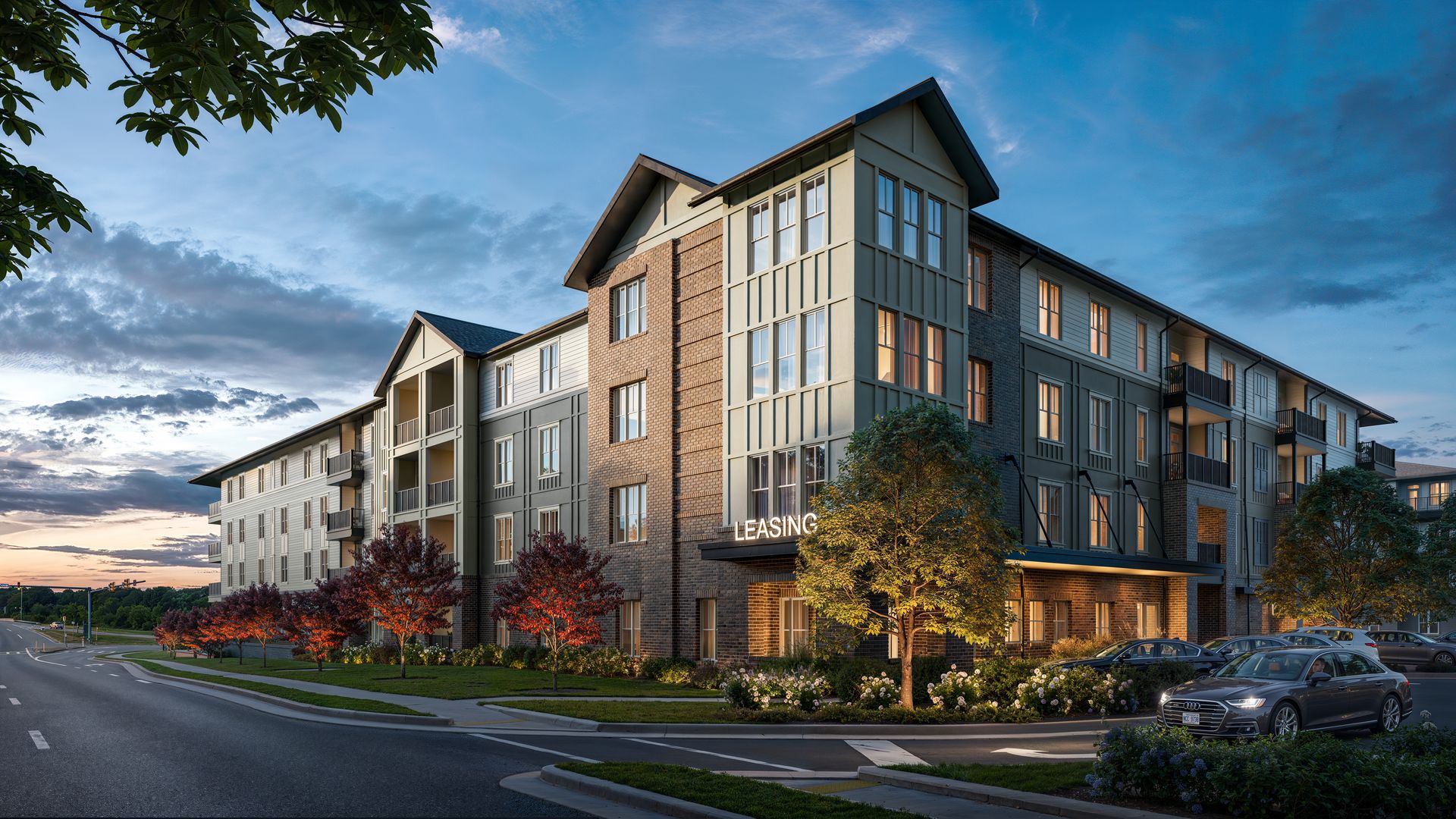 Modern four-story apartment building with brick and gray siding, balconies, and lit windows. A LEASING sign at the entrance; cars line a curved street at dusk, with trees and landscaping.