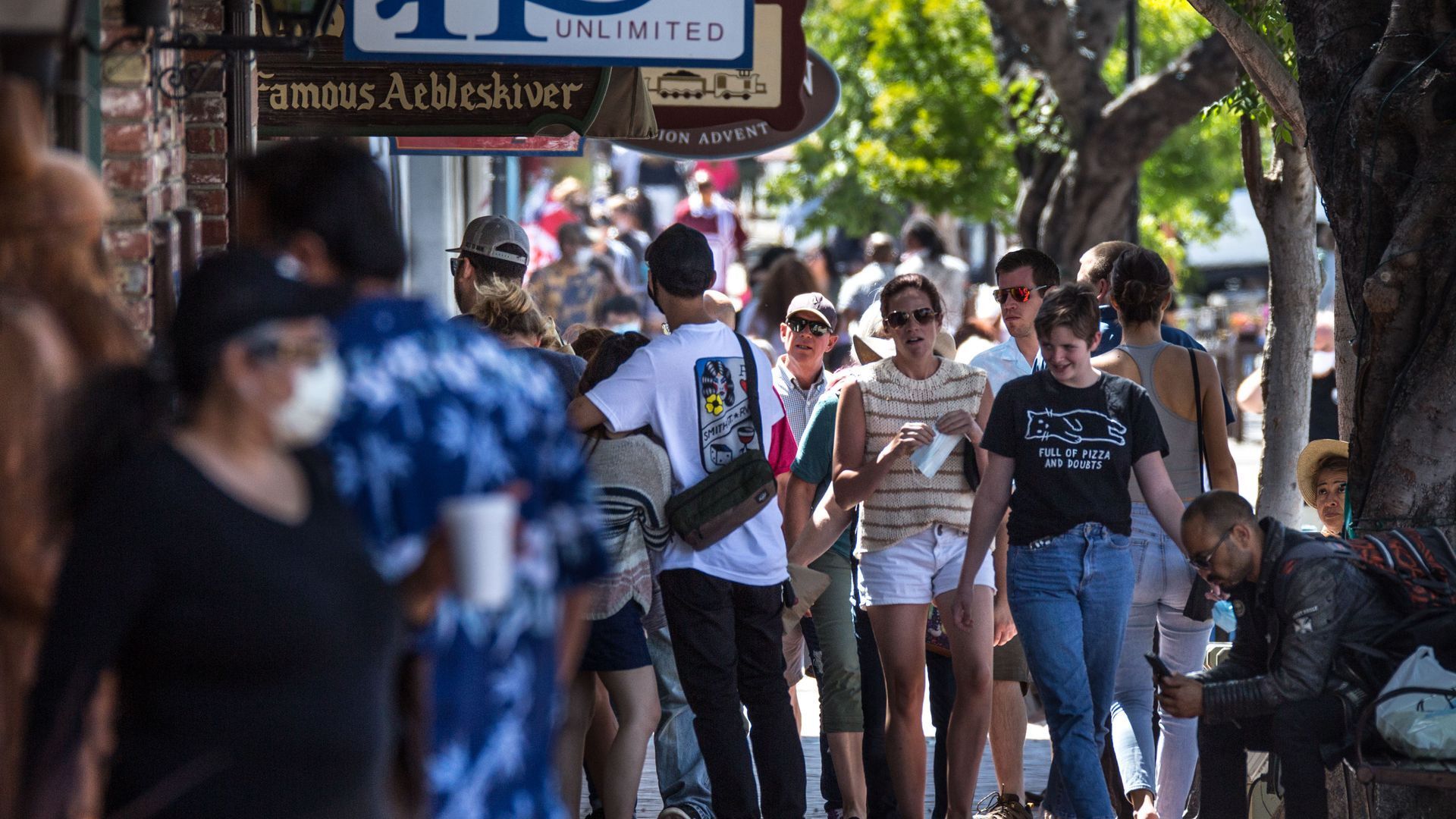 A crowd of people, some wearing face masks, walk through the streets of Solvang, California.