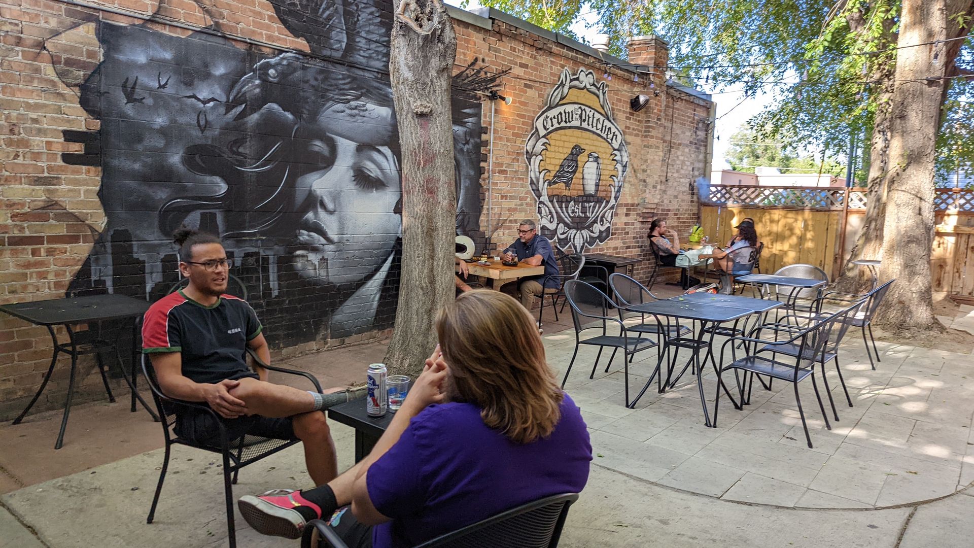 Two men sit on a patio near a mural.
