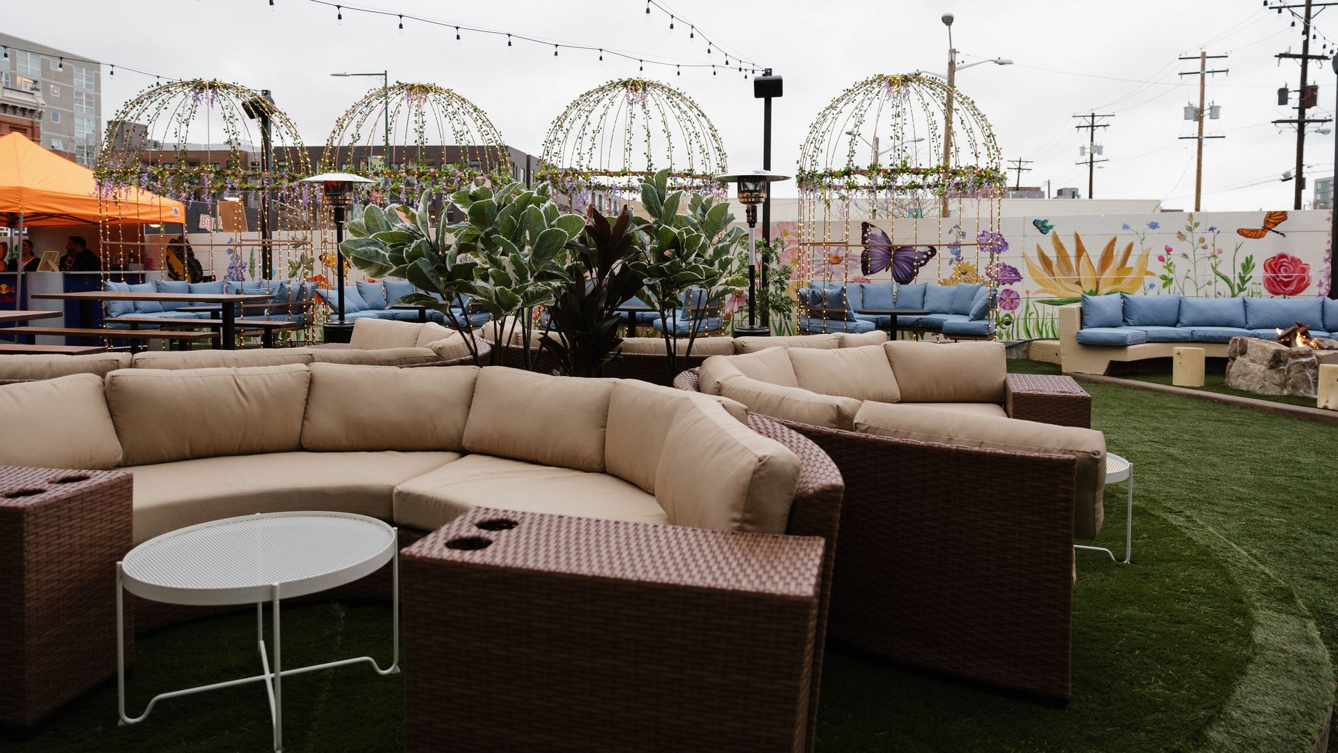 An open-air patio with large, beige lounging sofas, and large birdcages and fake grass. White walls in the background are painted with butterflies and flowers.  