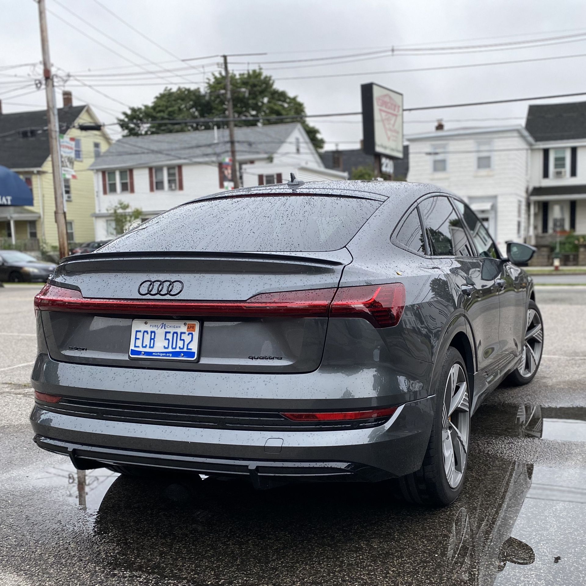 A photo of a gray Audi E-Tron Sportback, taken from the rear of the car, in a parking lot.