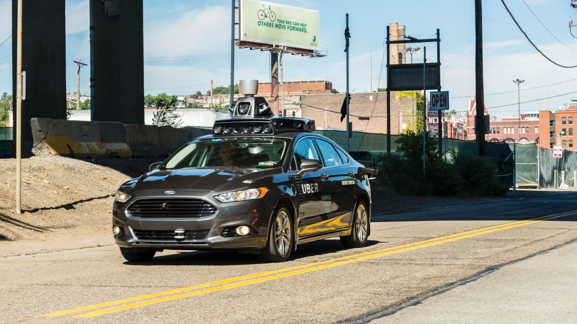 A black car drives down a sunny two-lane street