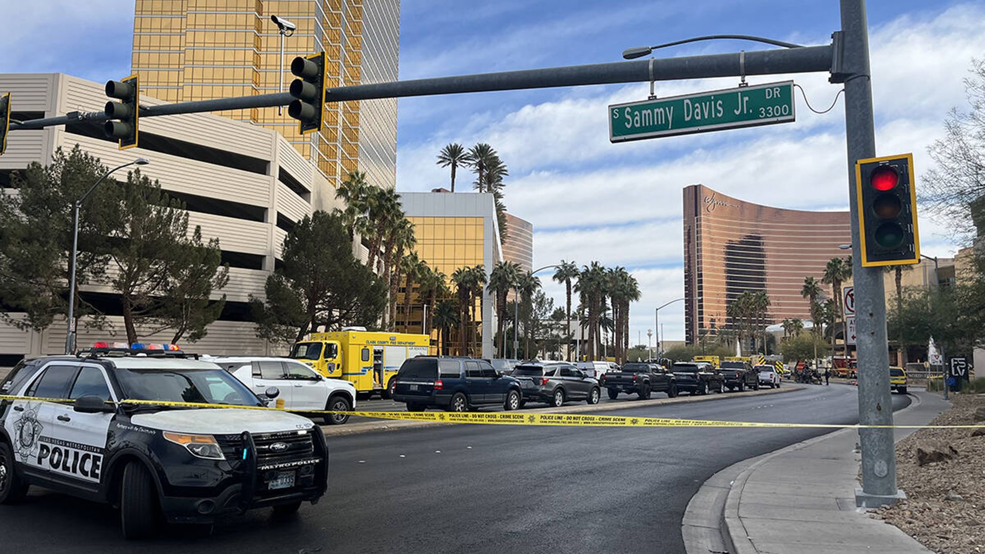 A police car parked behind a yellow police tape along a road, with several shiny hotel buildings in the background. 
